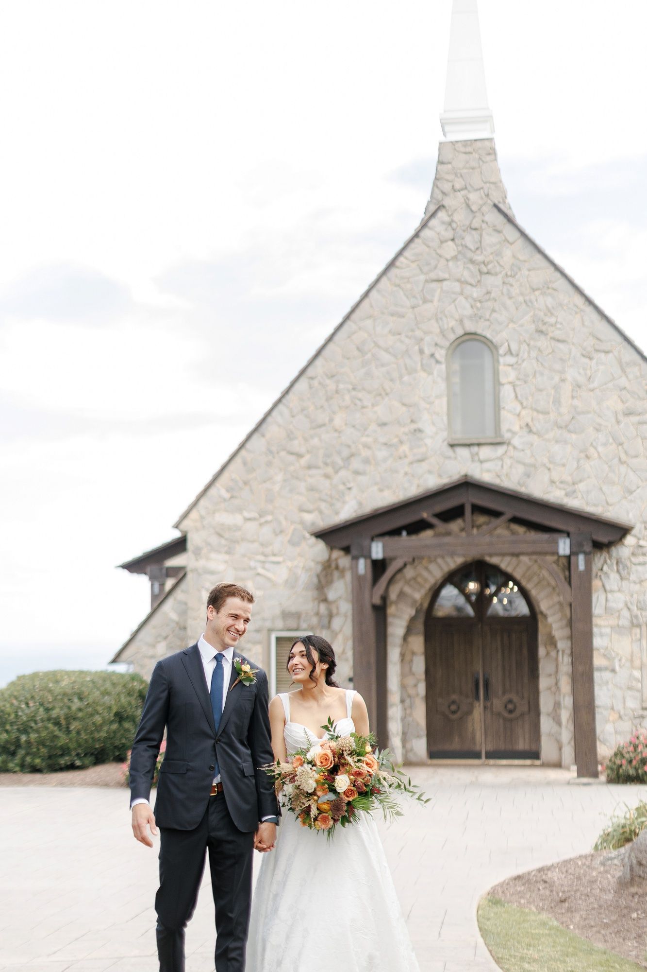 A couple shares a romantic moment outside a beautiful stone church with rustic wooden doors on their wedding day.