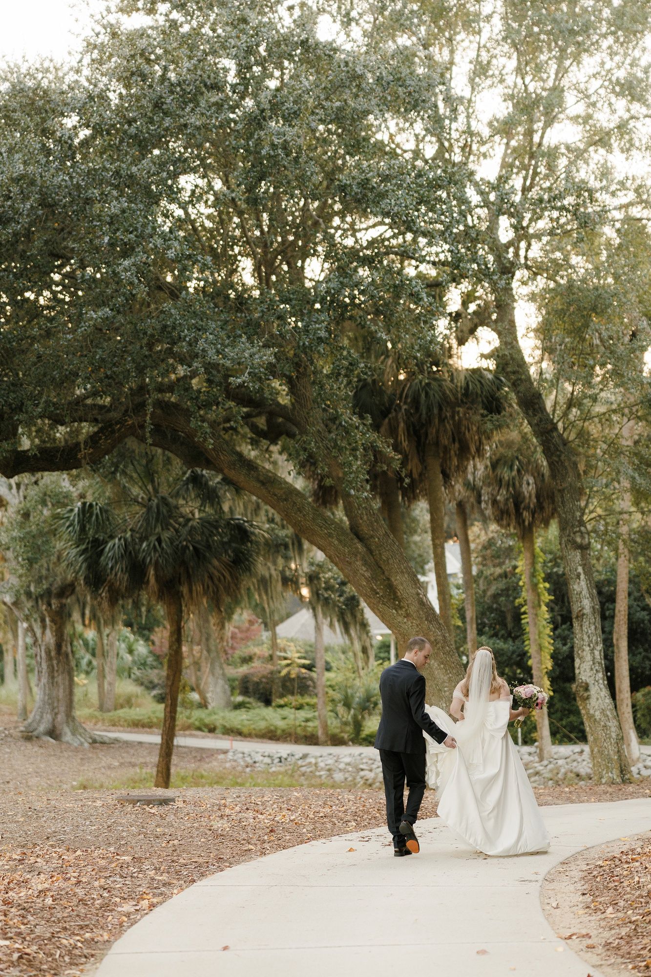 Couple walking through a romantic oak tree grove with Spanish moss during their wedding photoshoot.