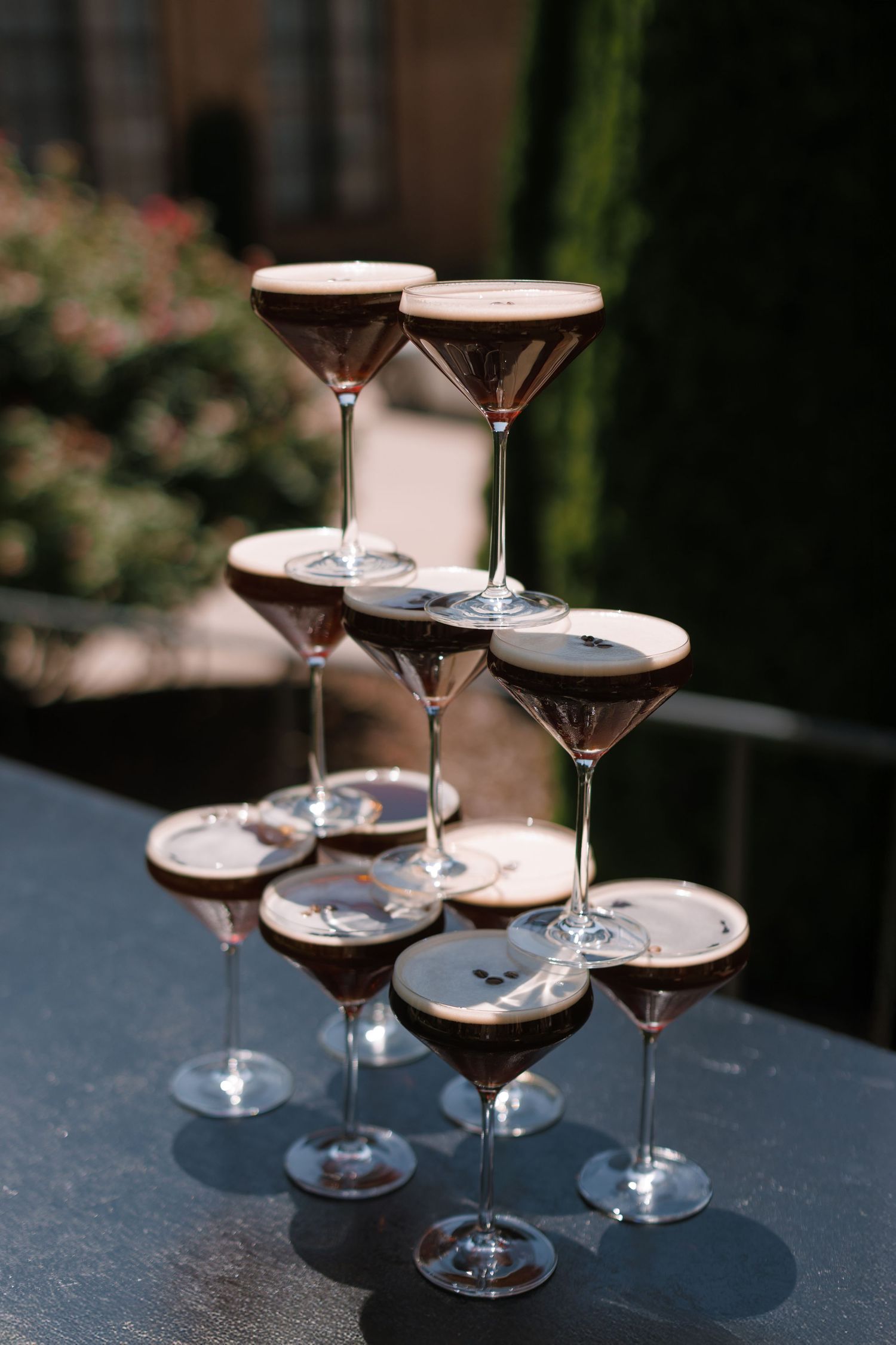 A pyramid tower of espresso martini cocktails stacked on a table at an outdoor event.
