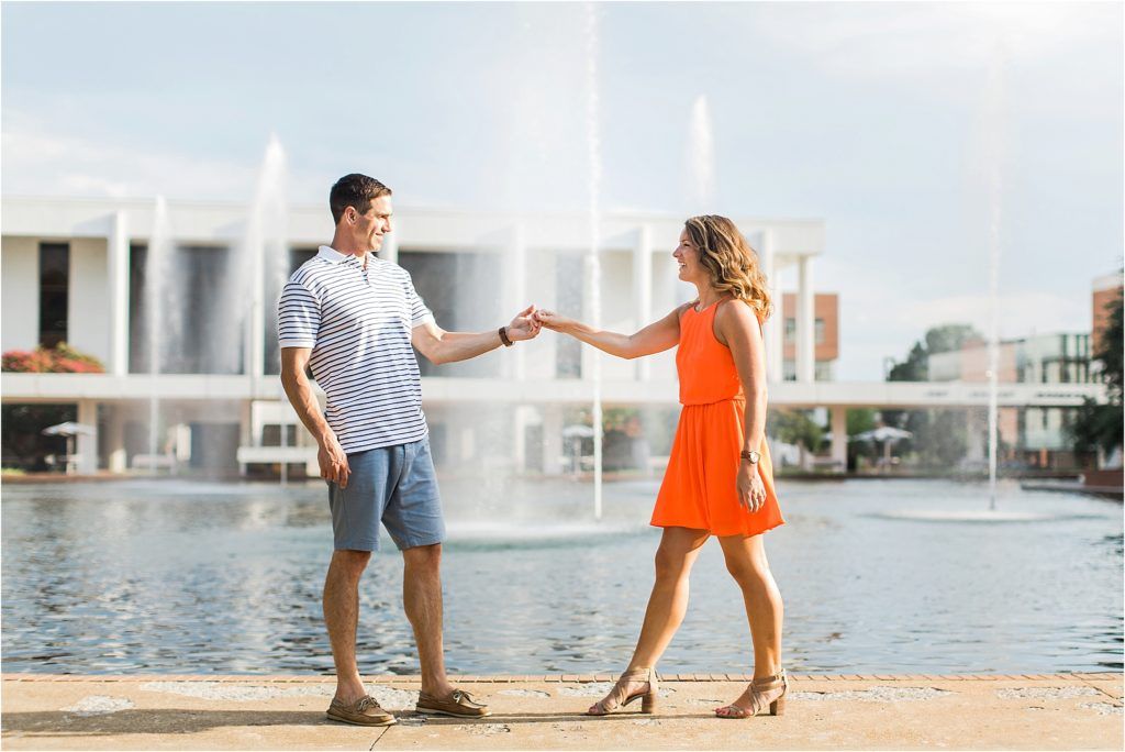 Couple dancing by fountain in casual summer outfits during engagement session.