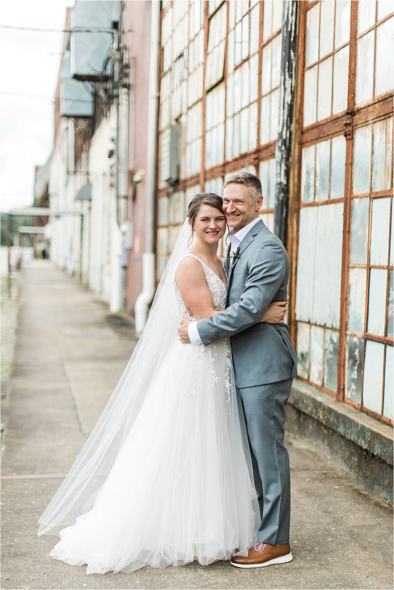 Elegant wedding portrait against industrial building with large windowpanes.