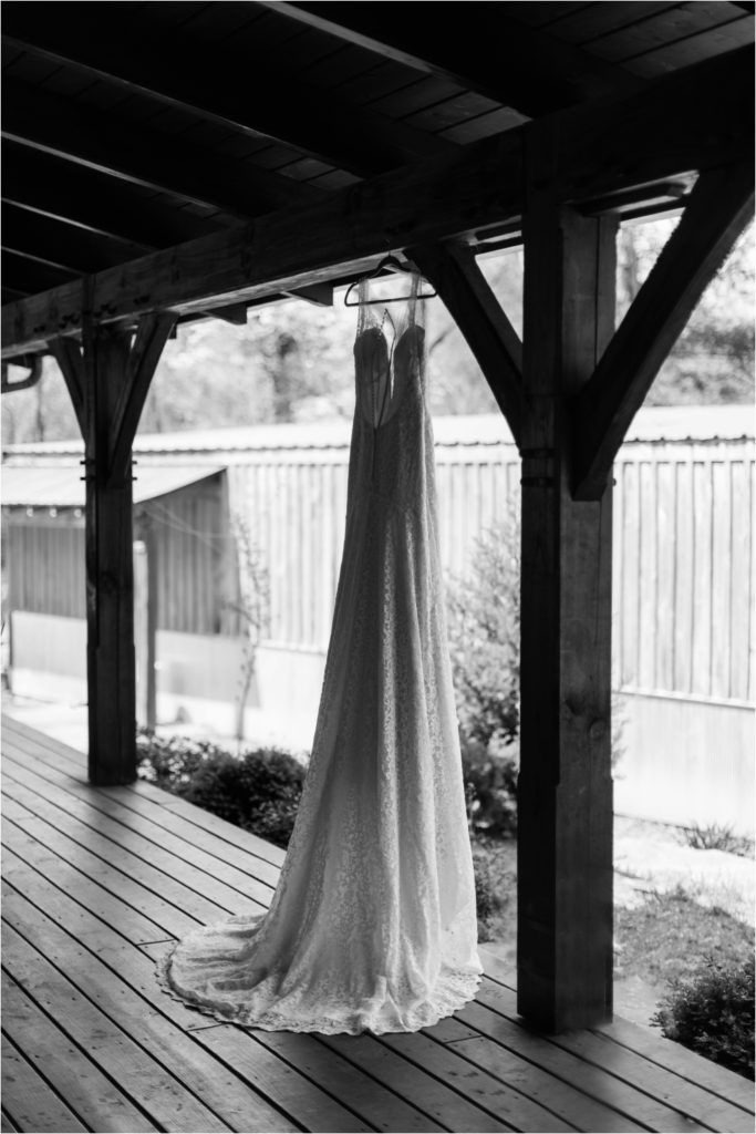 Elegant white wedding dress hanging from wooden beams on a covered porch.