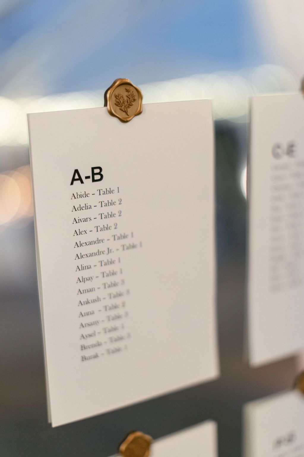 Wedding seating chart card with alphabetical guest listings and gold wax seal.