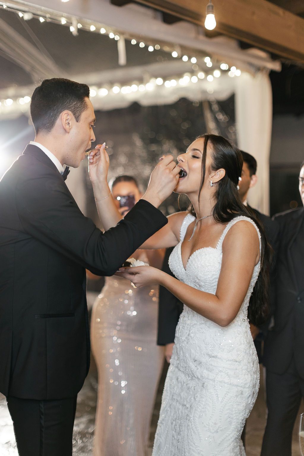 Wedding couple sharing cake during traditional cake feeding moment at reception.