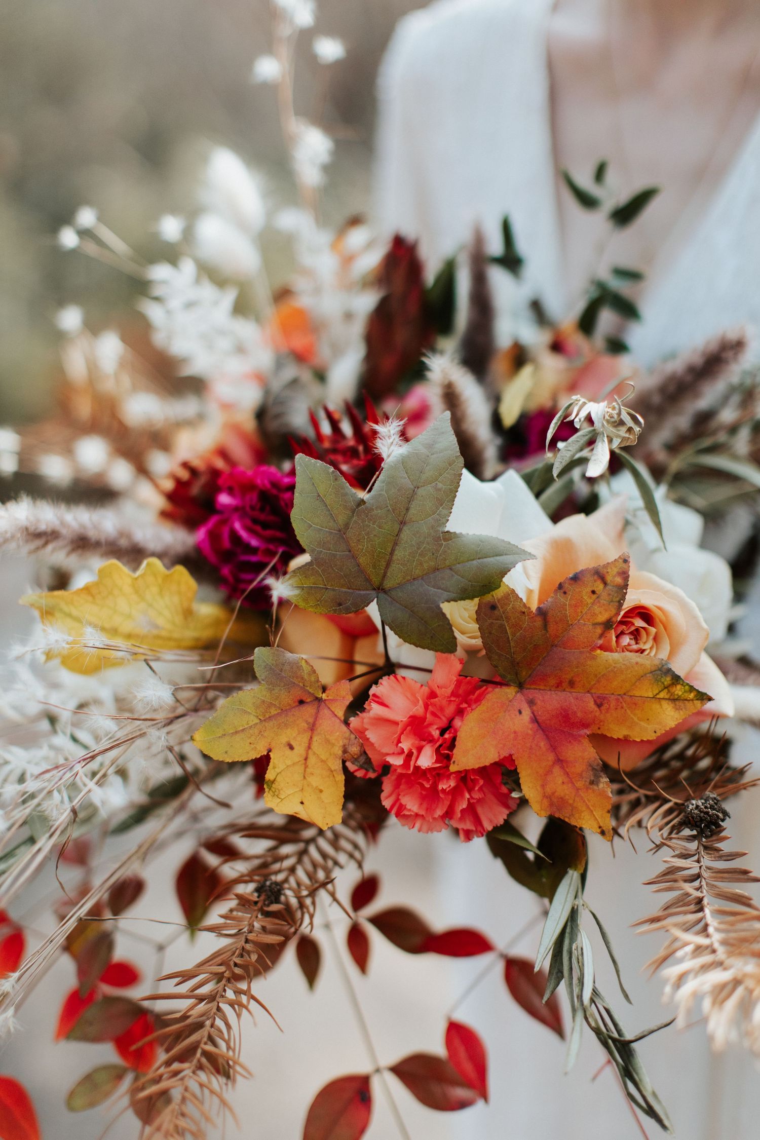 Autumn-inspired wedding bouquet with maple leaves, roses, and dried elements in warm fall colors.