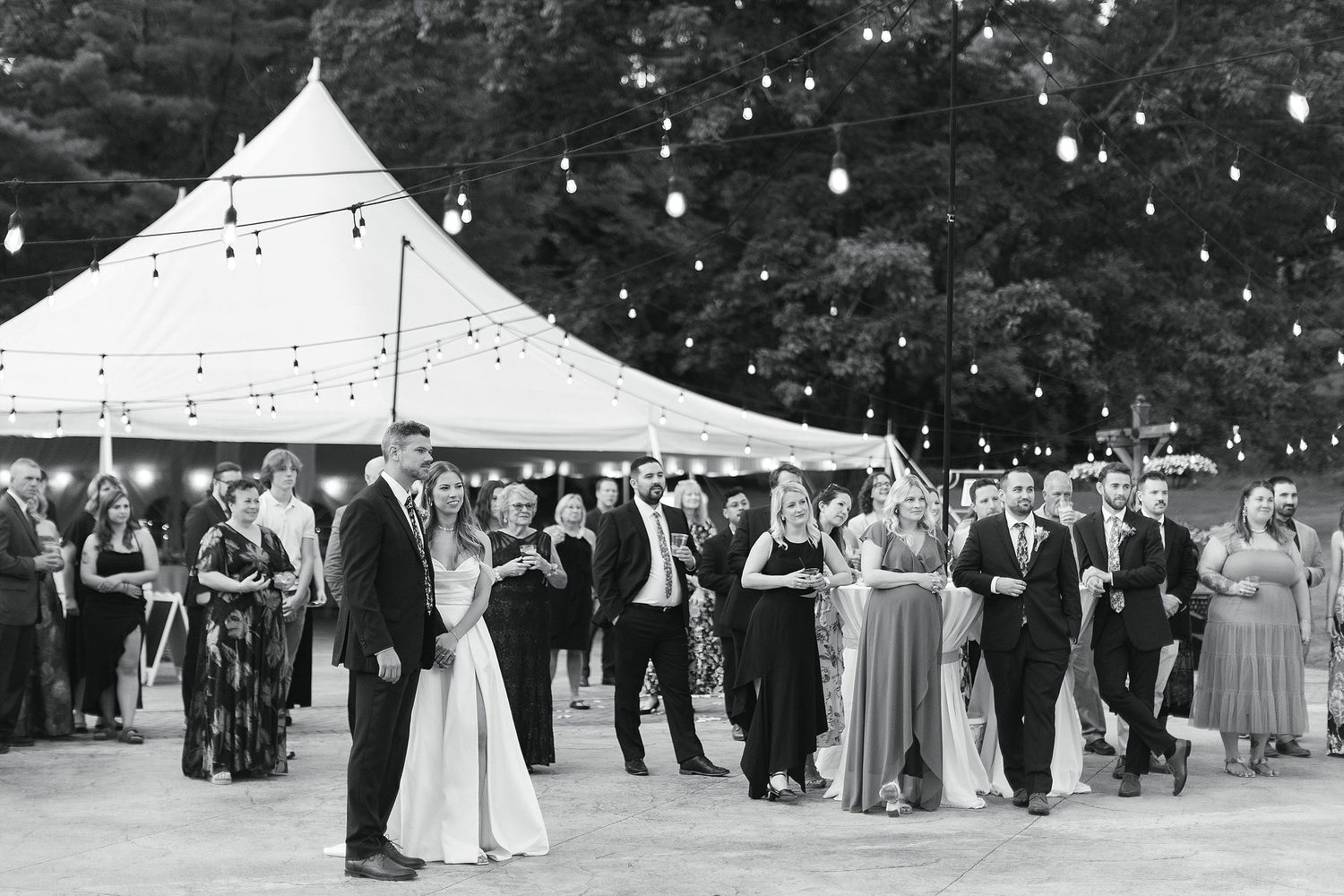 Wedding reception under white tent with string lights and guests dancing.