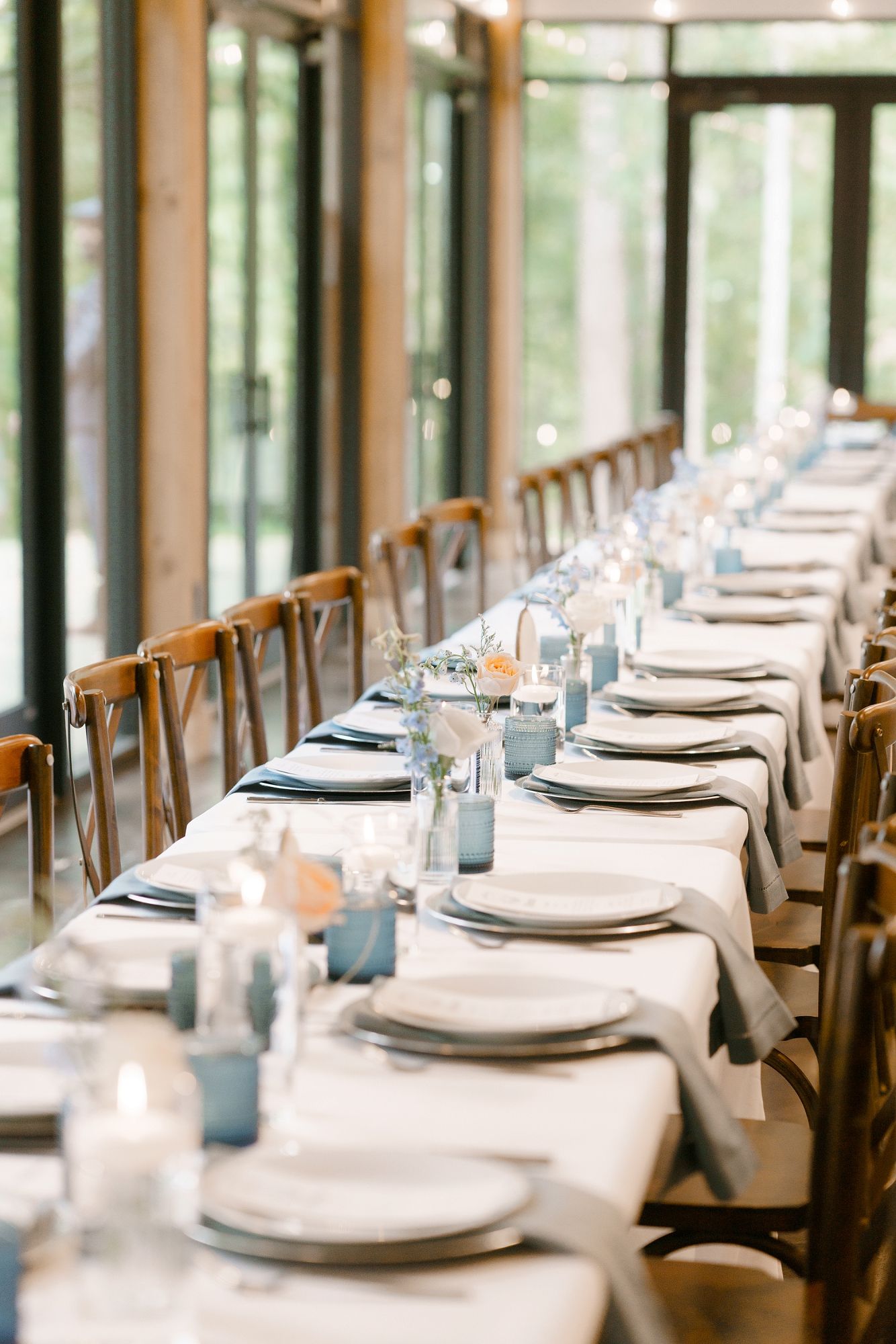 Elegant long banquet table with blue napkins, white linens, and wooden cross-back chairs in a bright venue.