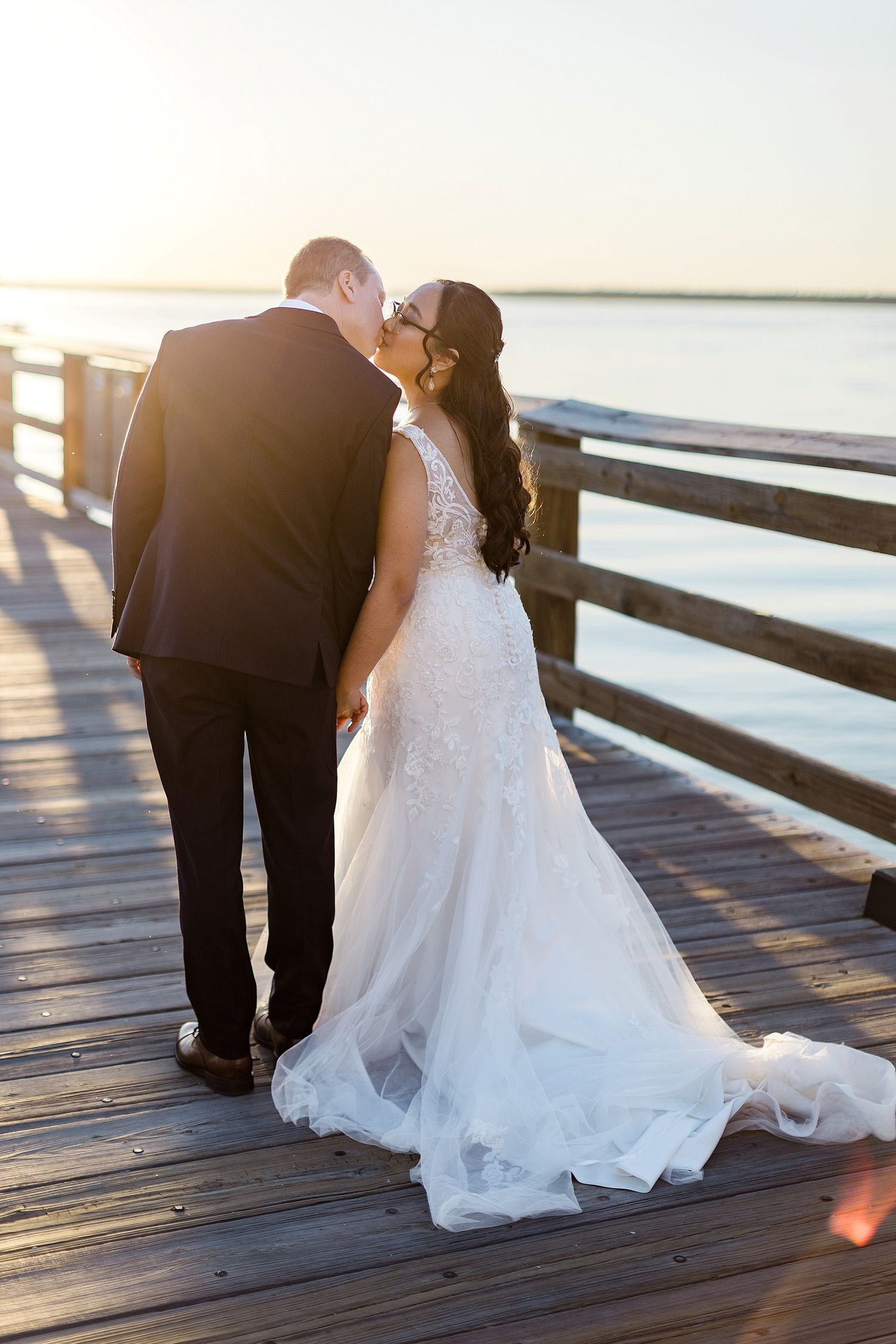 A romantic sunset moment on a wooden pier with flowing white wedding dress.