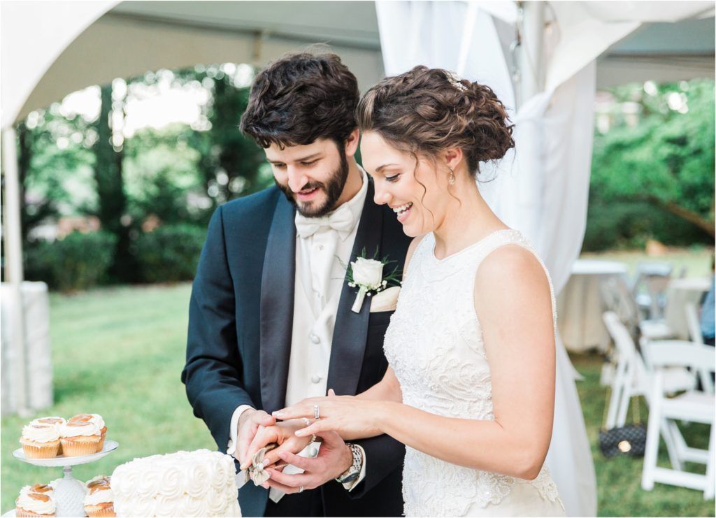 Newlyweds cutting their wedding cake together under an outdoor tent.