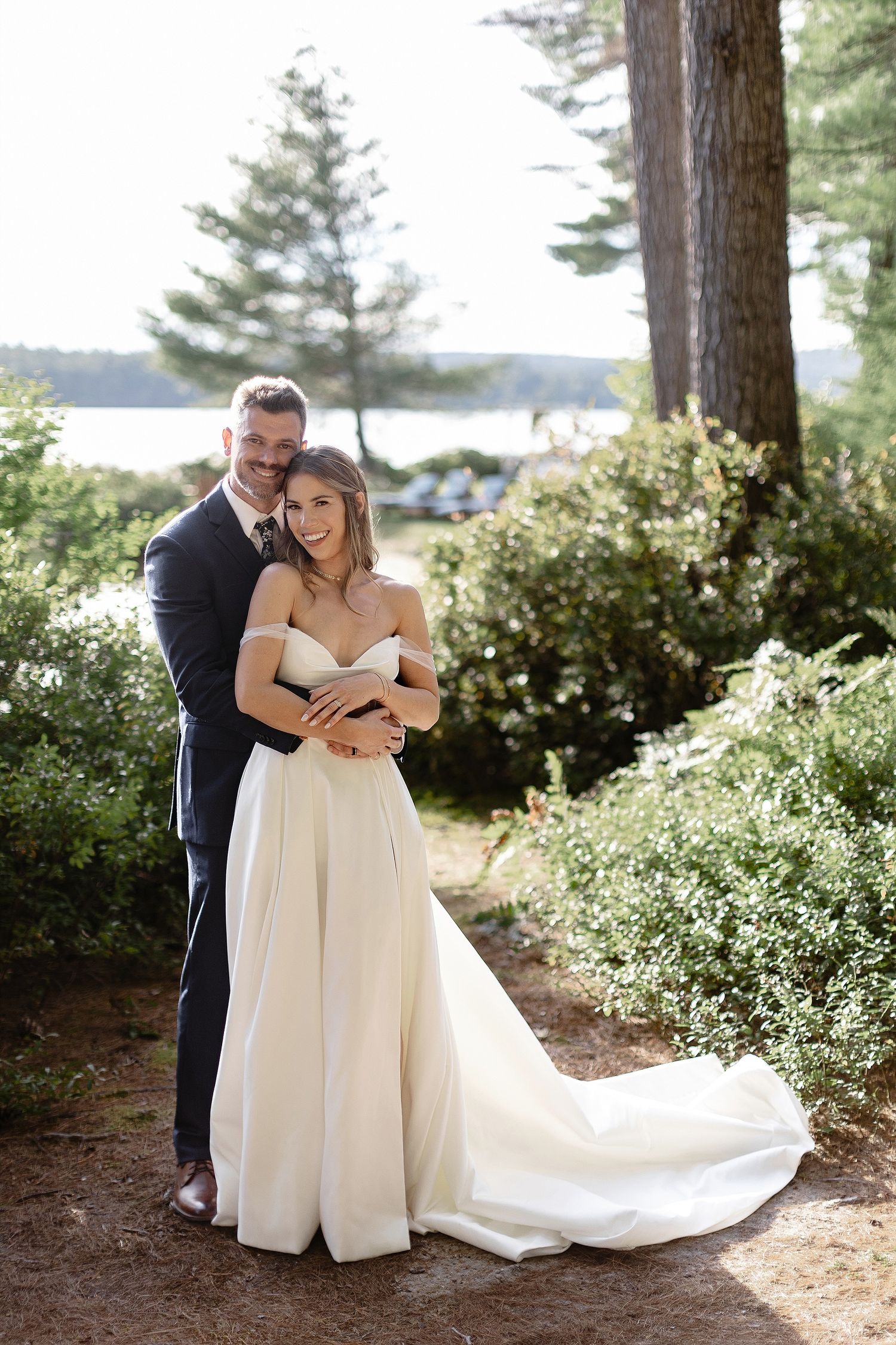 A romantic wedding portrait among pine trees with a lake view in the background.