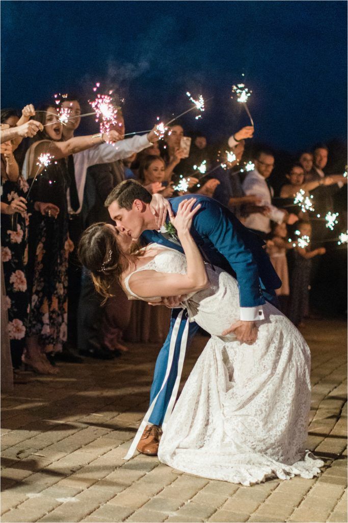 Romantic dip kiss during sparkler exit at nighttime wedding celebration.