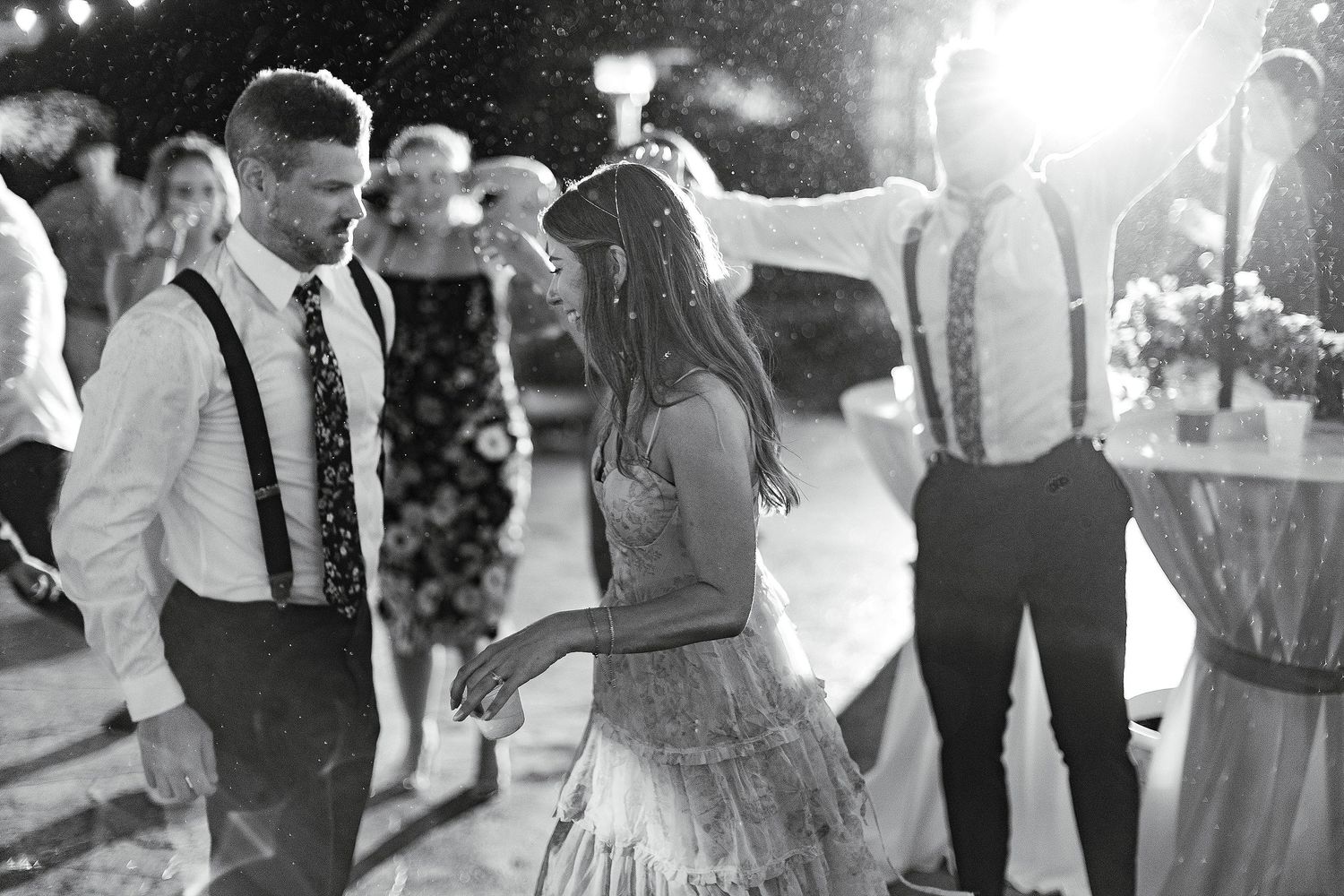 Black and white photo of guests dancing at an outdoor wedding reception under string lights.