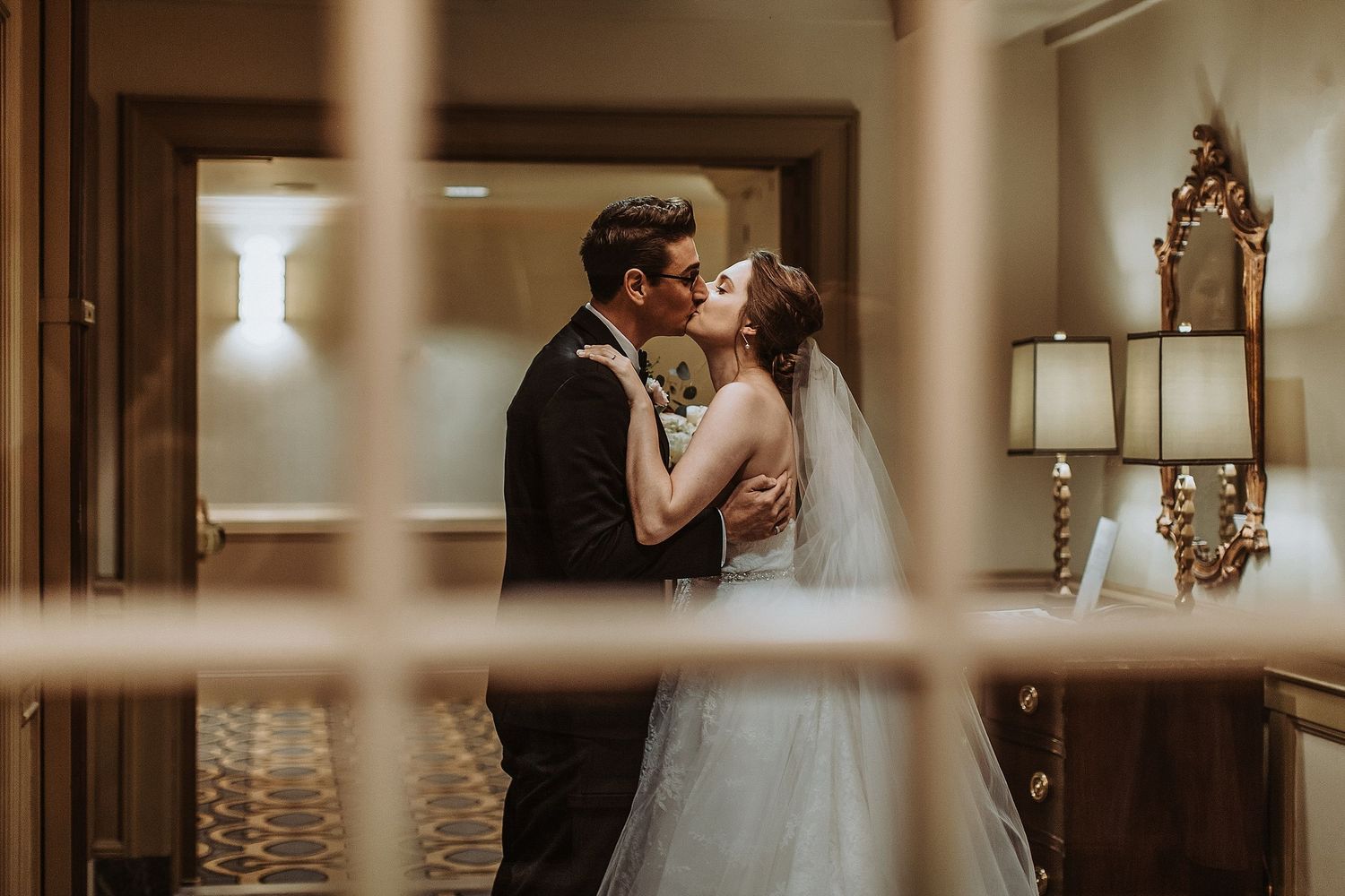 A romantic wedding moment captured through a doorframe in warm lighting.