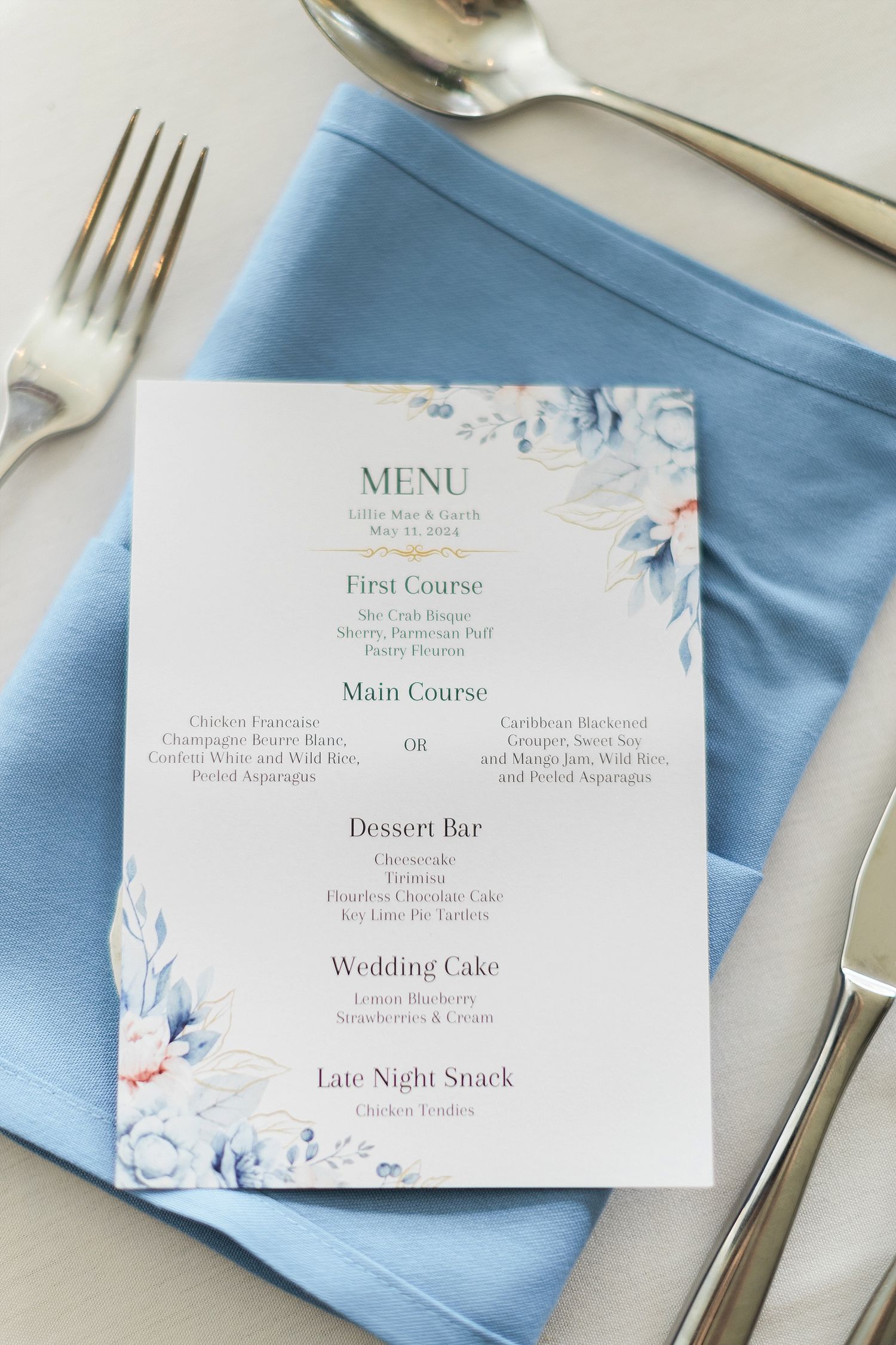 Wedding menu card with blue floral design placed on light blue napkin with silverware.