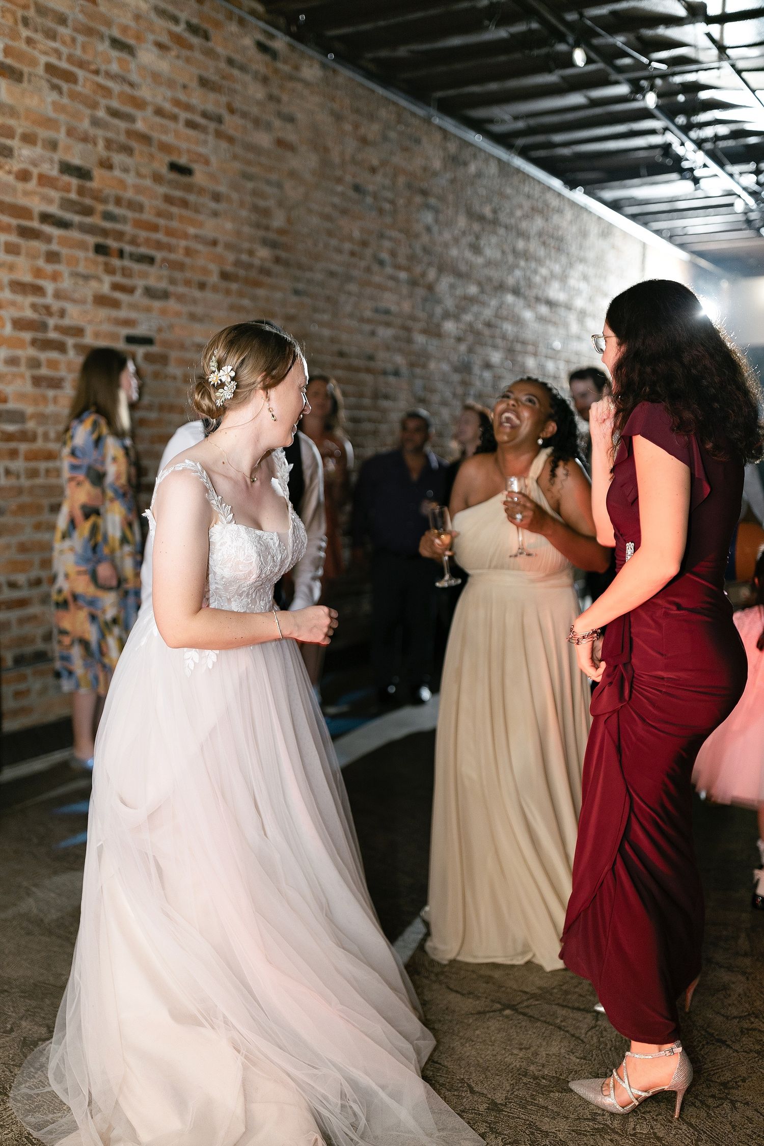 Wedding guests dance and celebrate together at a rustic brick-walled venue with moody lighting.