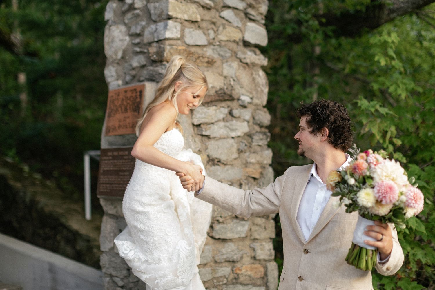 A bride and groom share a joyful moment together surrounded by lush greenery and rustic stone architecture.