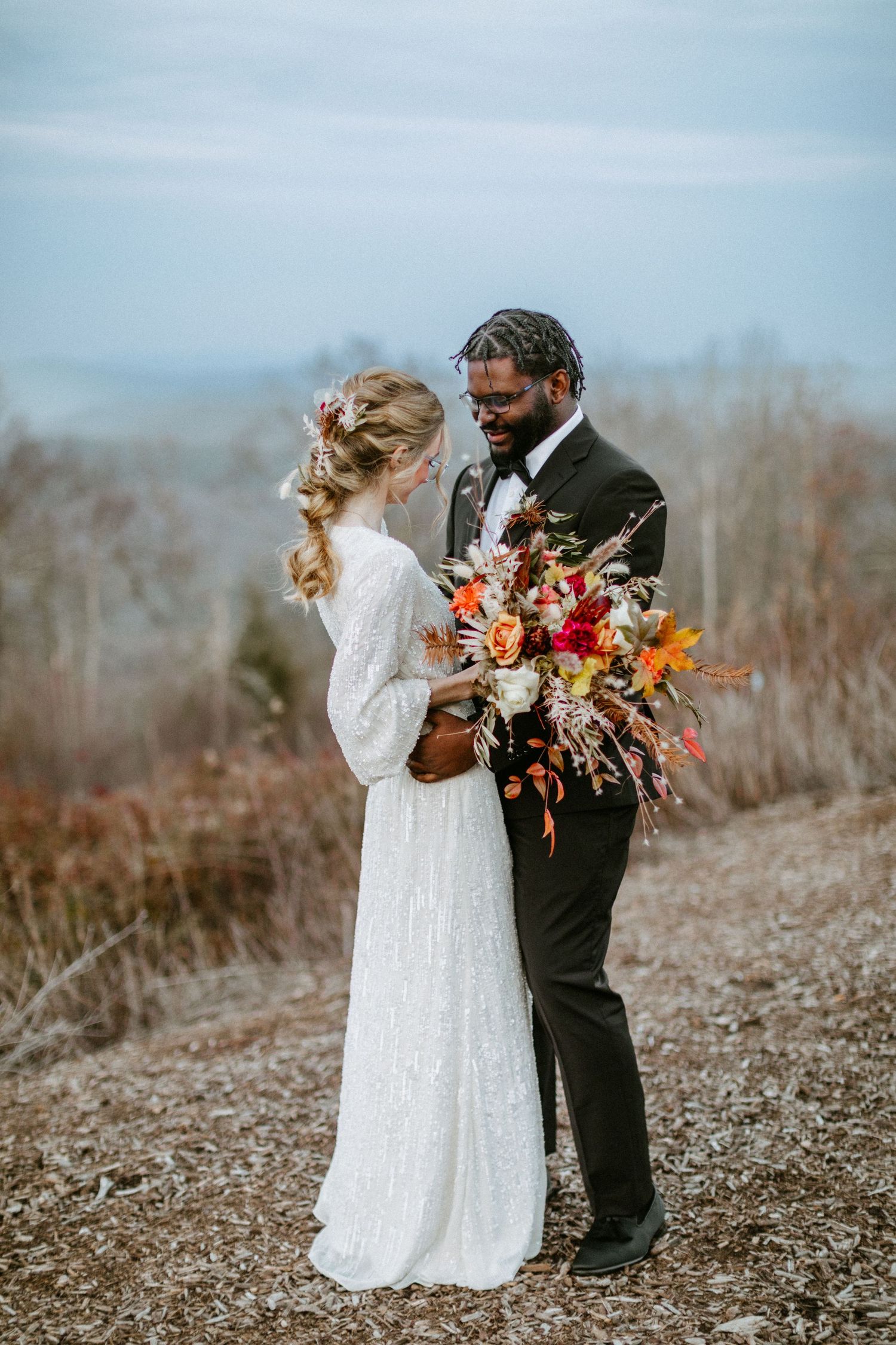 Romantic wedding portrait with a couple and colorful fall bouquet against mountain backdrop.
