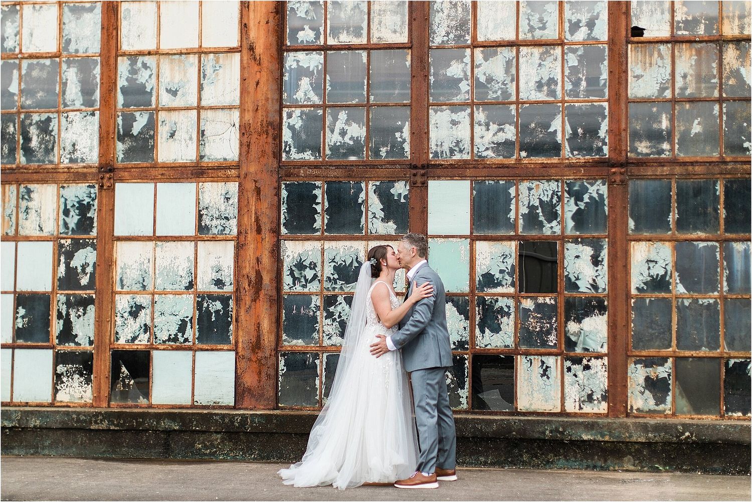 Wedding portrait against vintage industrial windows with peeling paint.