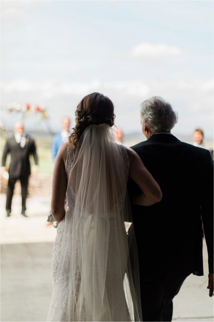 Intimate moment captured from behind as bride walks with escort during outdoor ceremony.