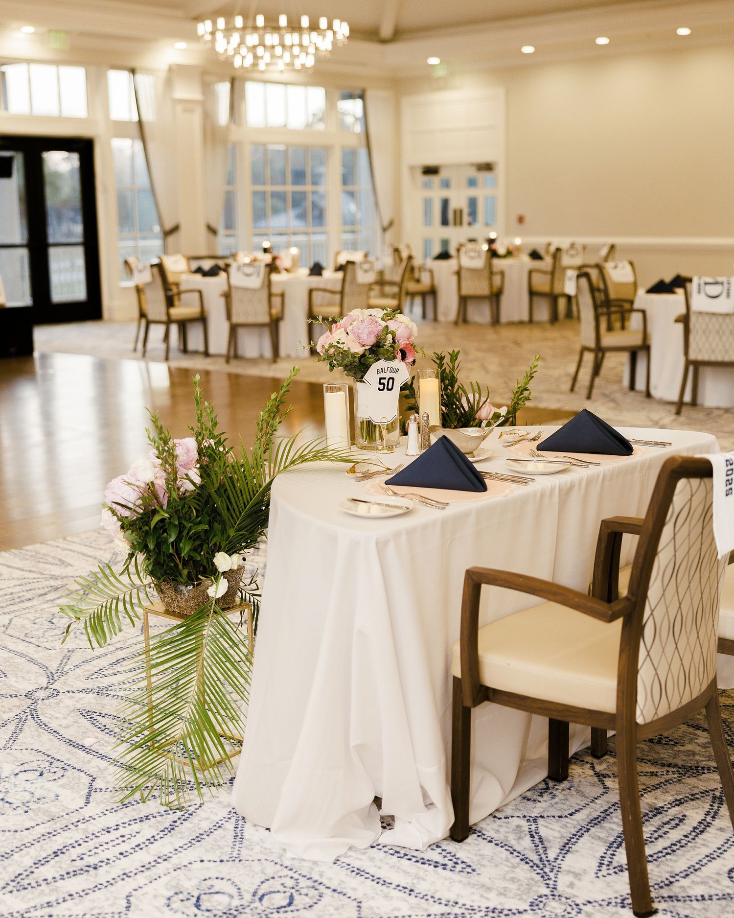 An elegant wedding reception venue with white tablecloths, navy napkins and greenery centerpieces.