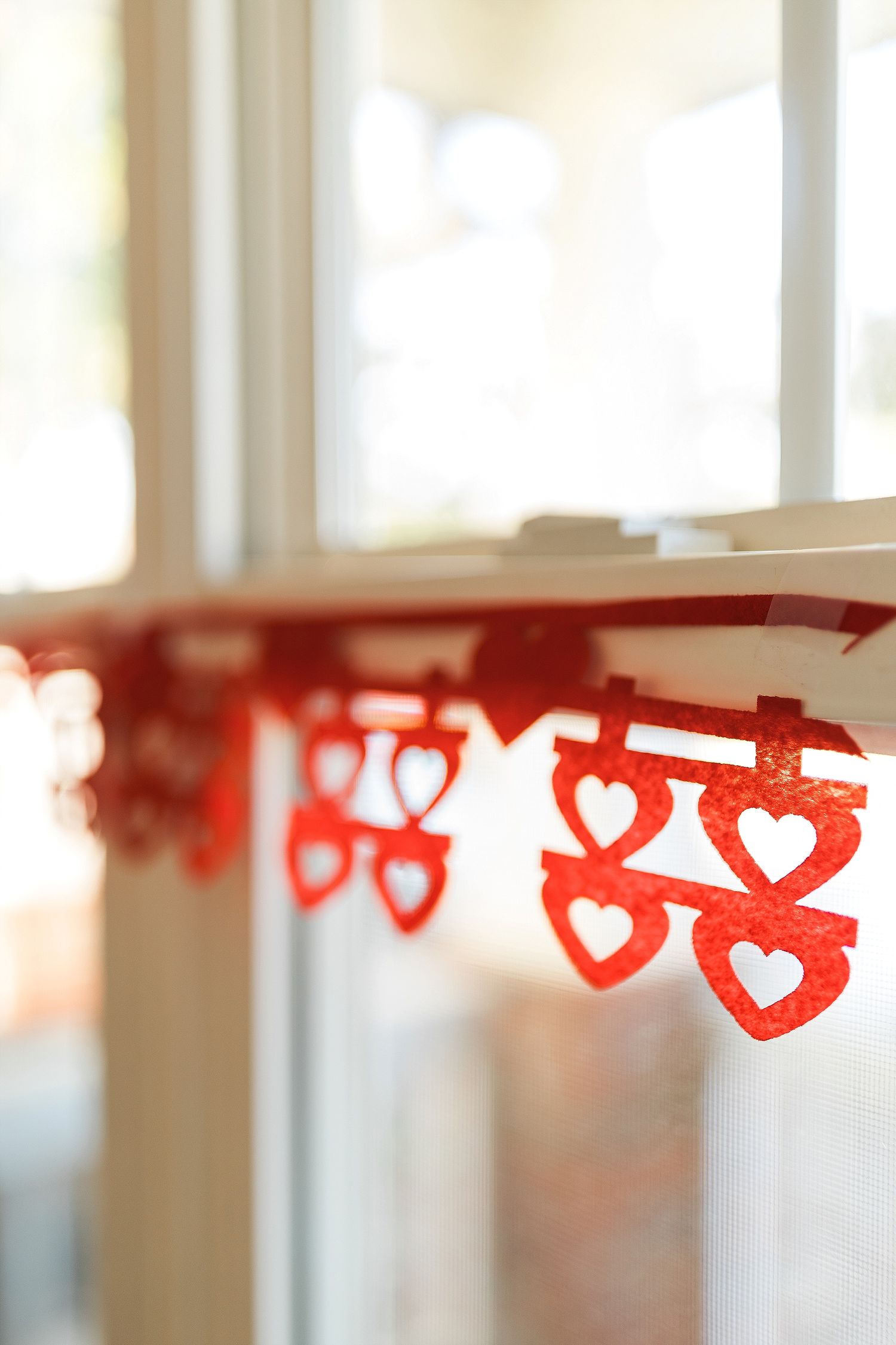 Red heart-shaped paper garland decorates a bright window frame creating a romantic Valentine's Day ambiance.