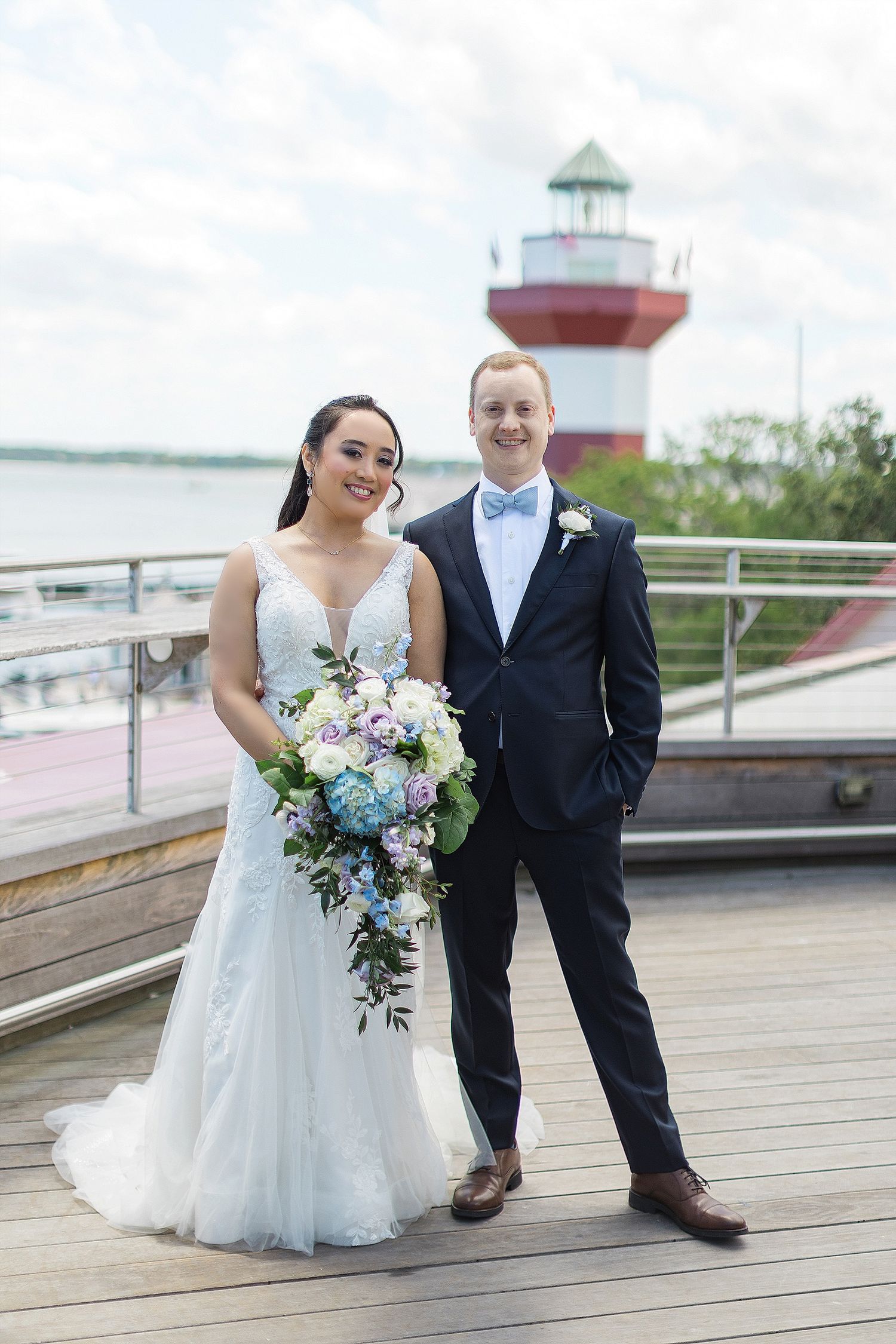 Wedding couple poses on boardwalk with iconic red and white lighthouse in background.