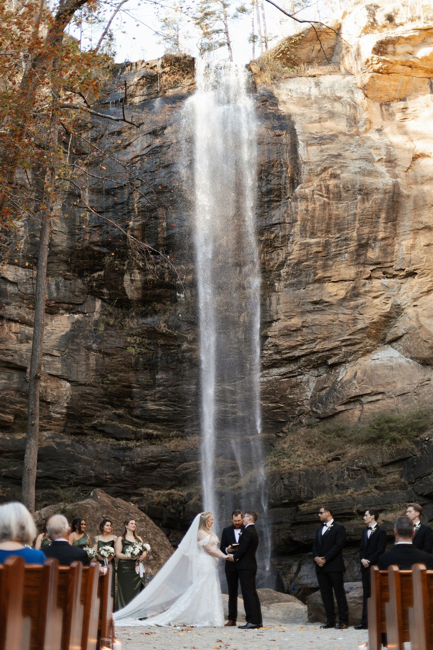 A stunning outdoor wedding ceremony takes place in front of majestic Toccoa Falls, cascading down tall rocky cliffs.