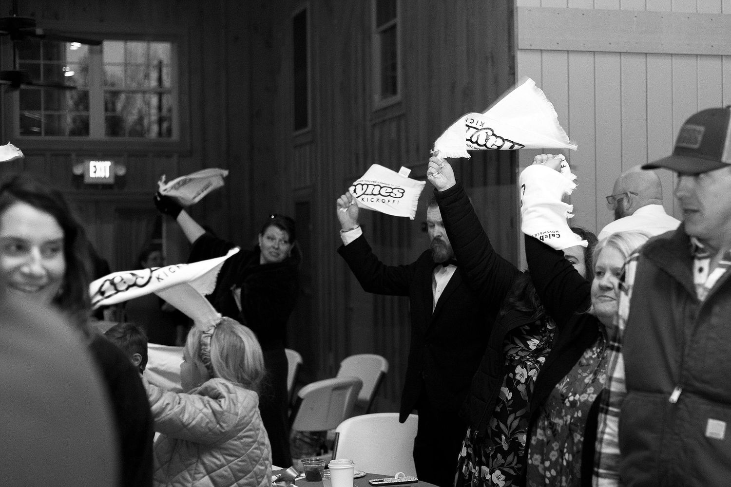 A crowd celebrates outdoors wearing paper hats and party attire in black and white photography.