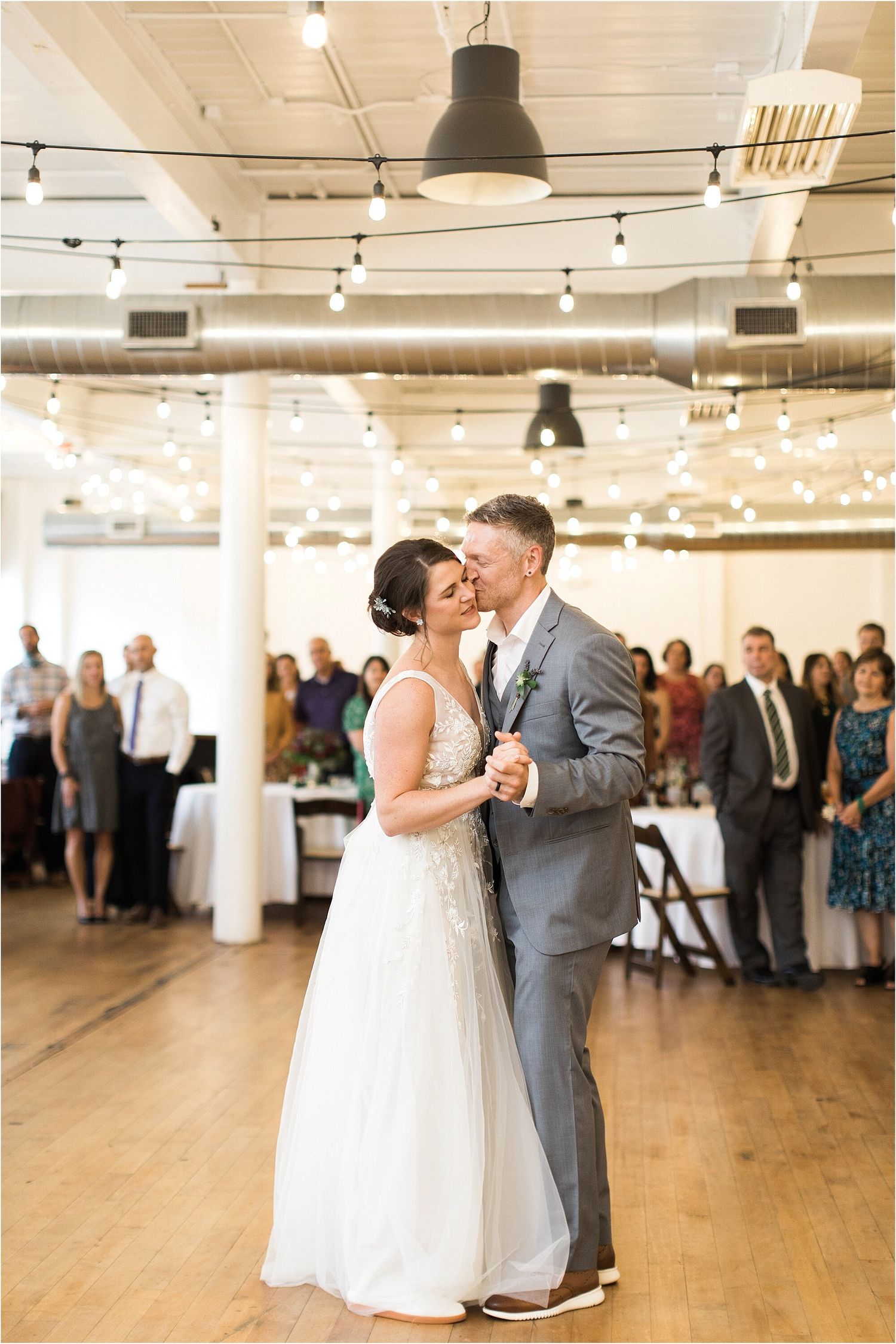 A couple dances in a modern reception venue with industrial lighting and exposed ceiling.