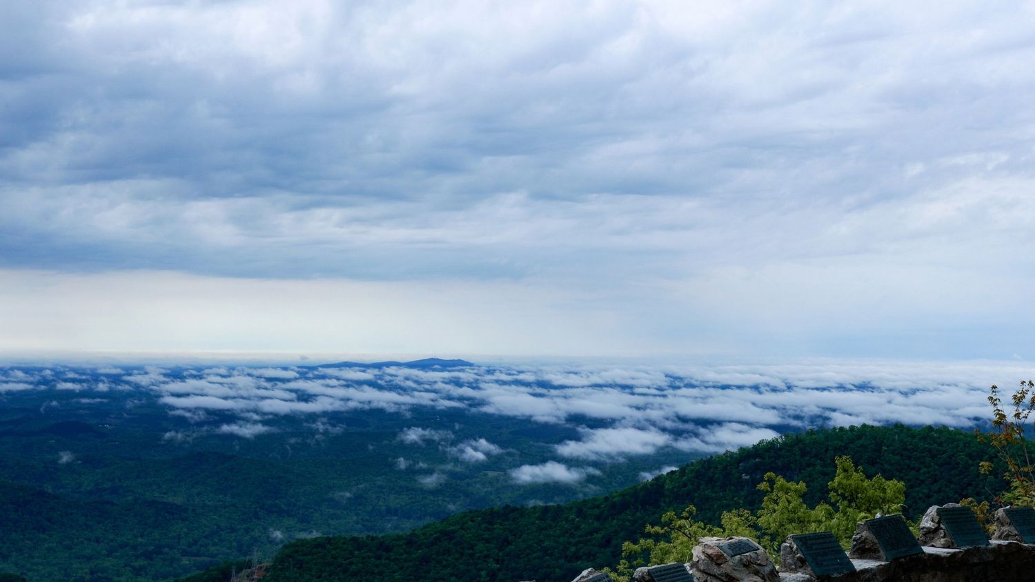 Scenic mountain landscape view with low-lying clouds stretching across rolling hills under a cloudy blue sky.