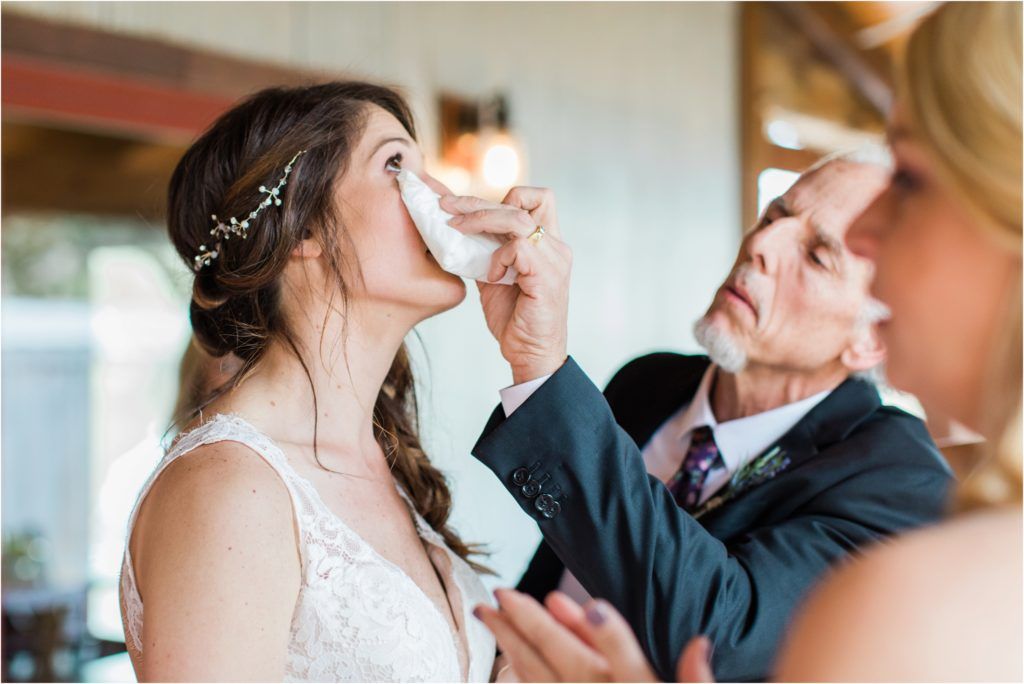 Emotional wedding preparation moment as someone dabs tears from the bride's face.