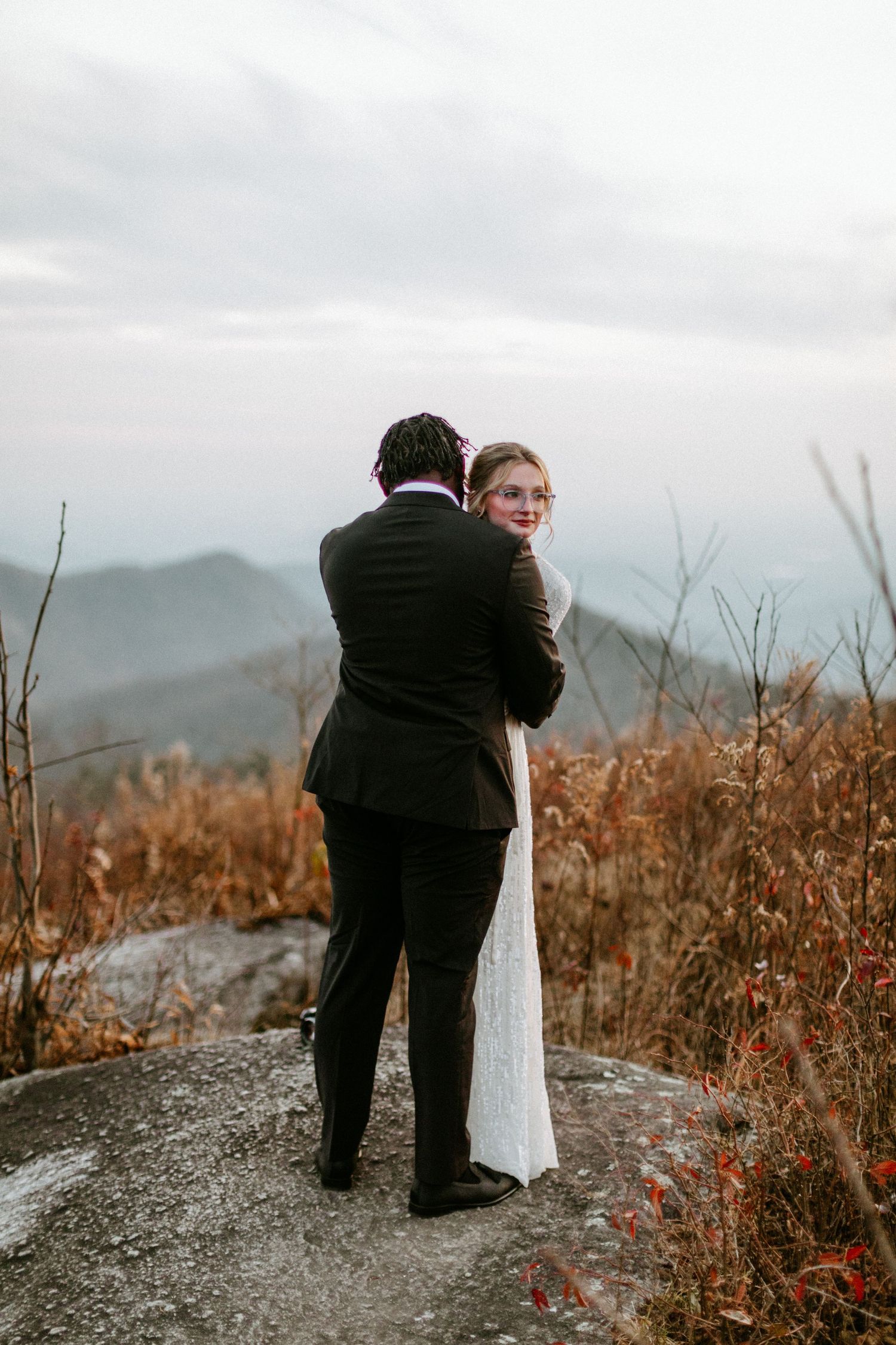 A romantic moment between newlyweds on a mountain peak with misty views in the background.