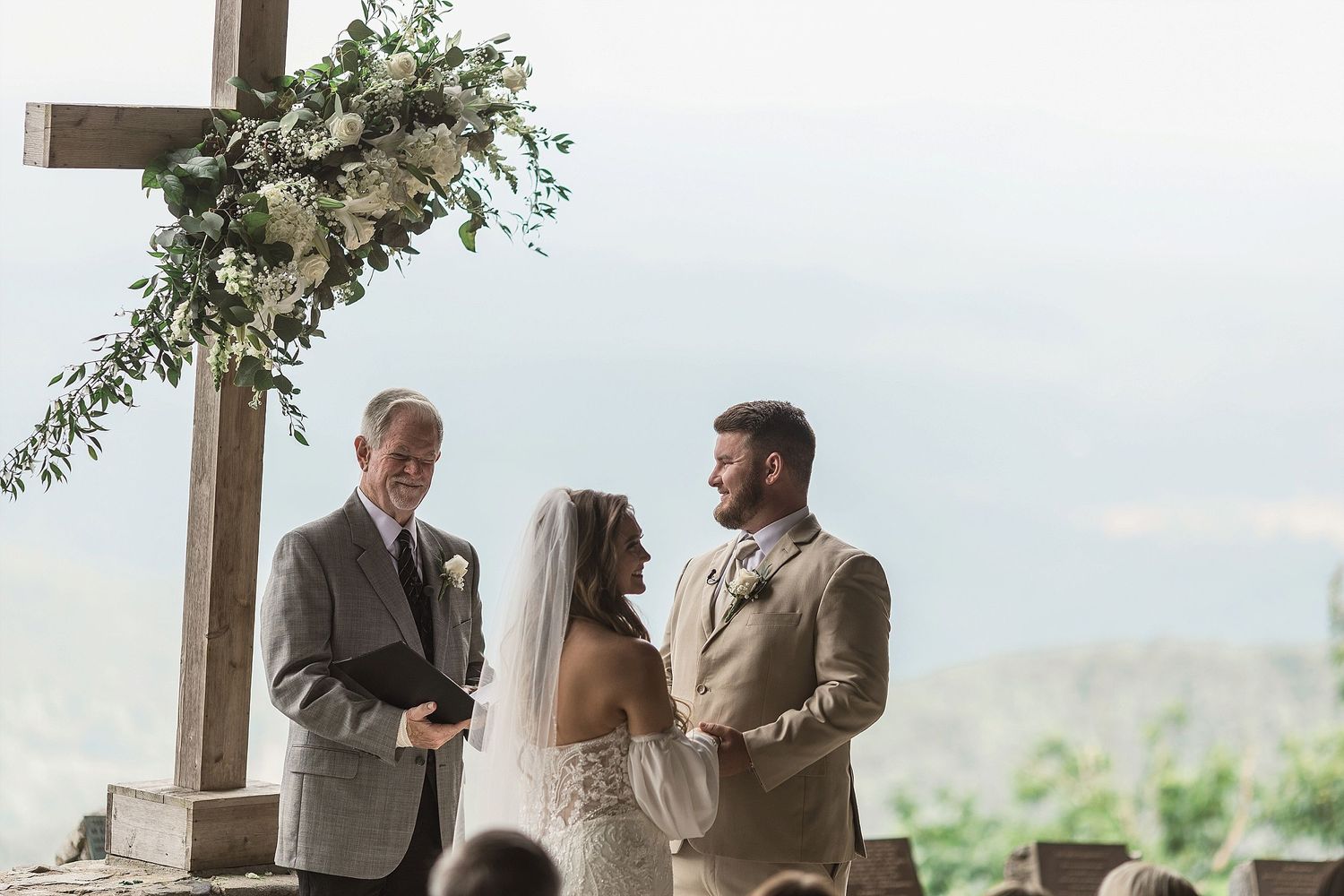 Wedding ceremony at scenic mountain overlook with wooden cross and floral decorations.