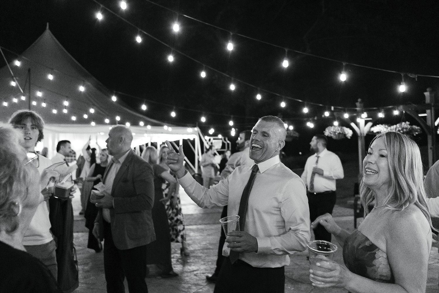 Wedding guests celebrate and dance under string lights at an outdoor reception.