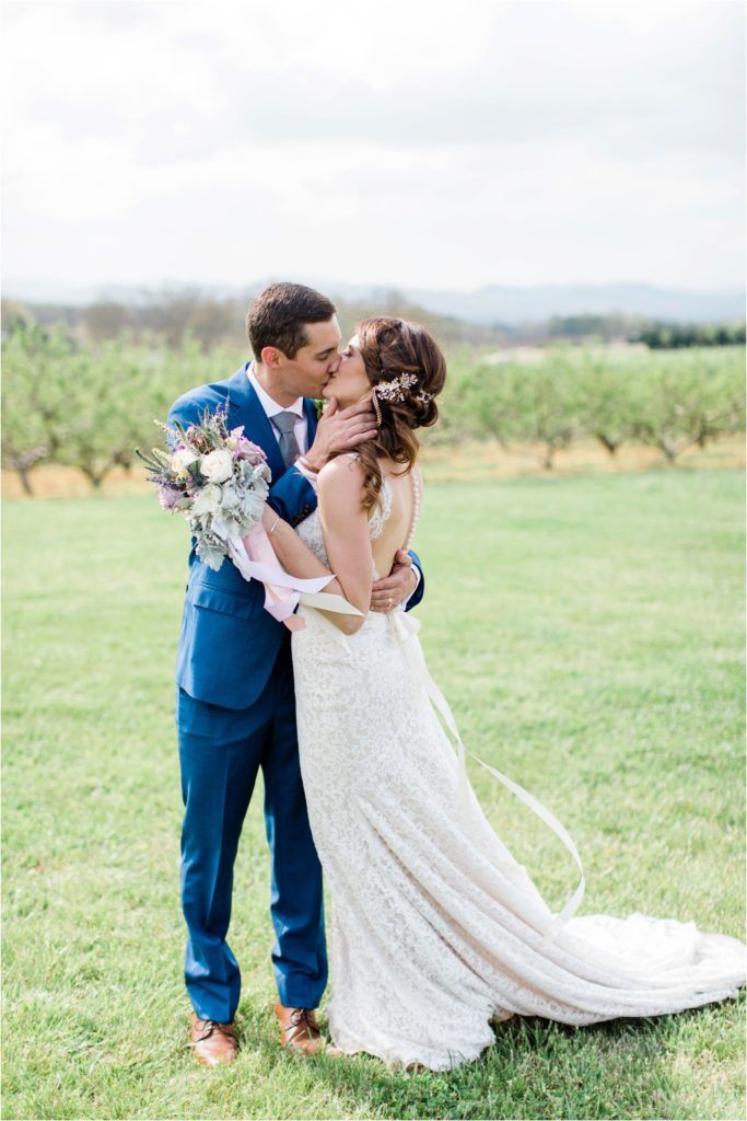 Romantic moment in vineyard with lace dress and blue suit against pastoral background.