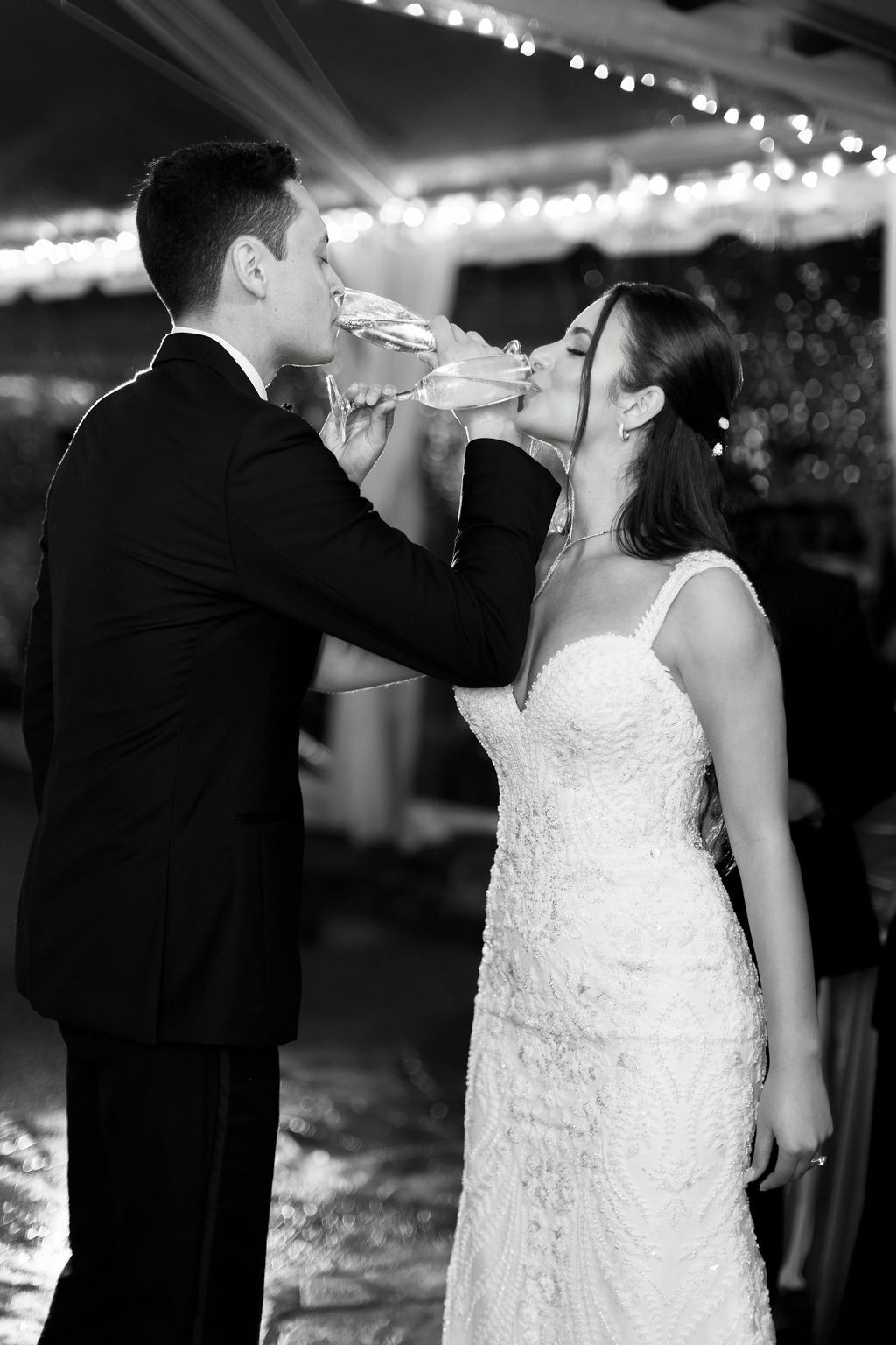Black and white photo of couple sharing champagne toast with crossed arms at wedding reception.