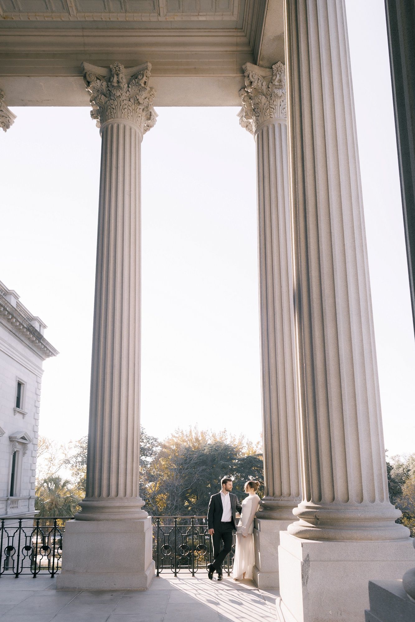 Classical white columns with ornate capitals frame a bright exterior view of a building's architectural details.