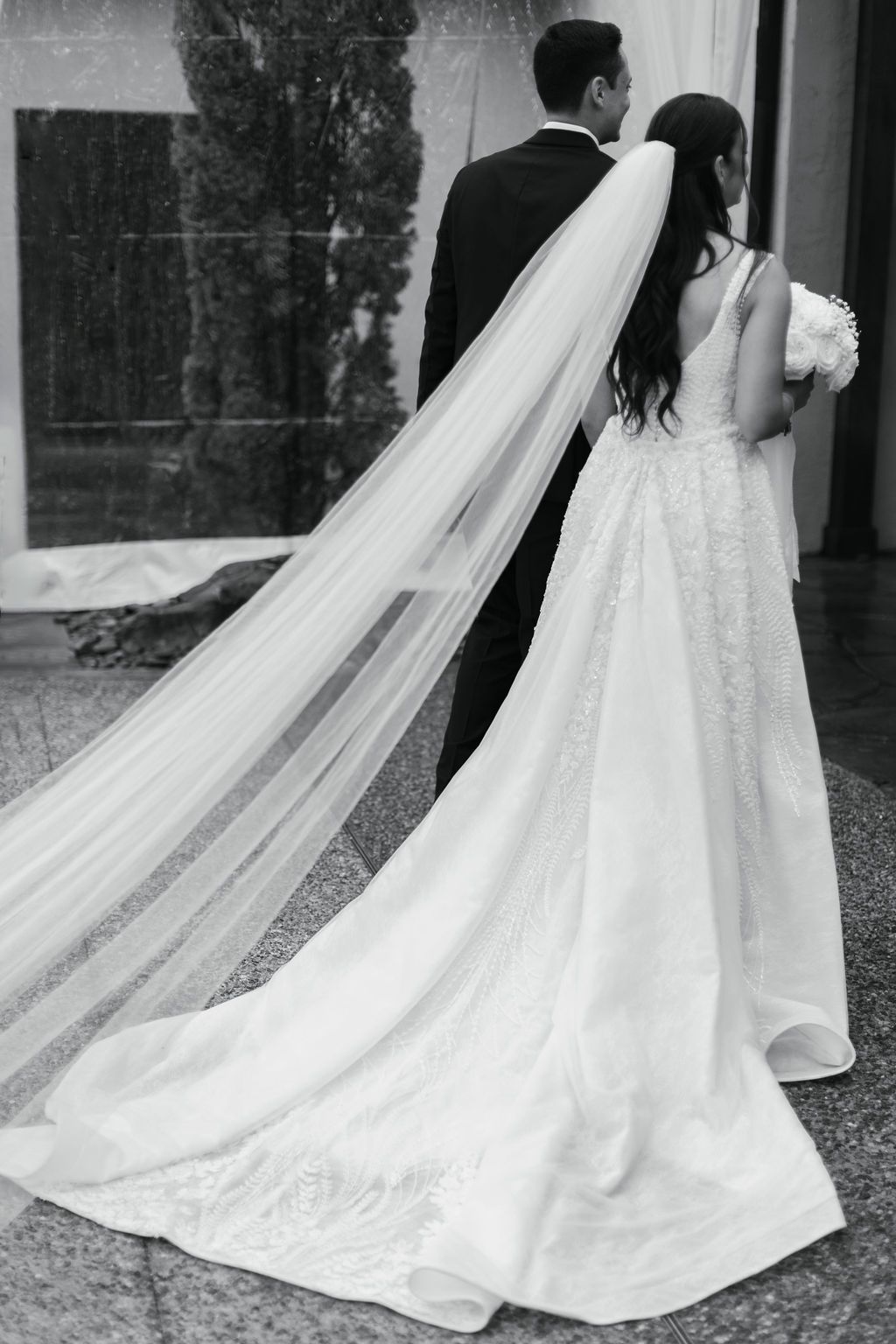 Black and white photo showcasing a long cathedral veil and elegant wedding gown train.