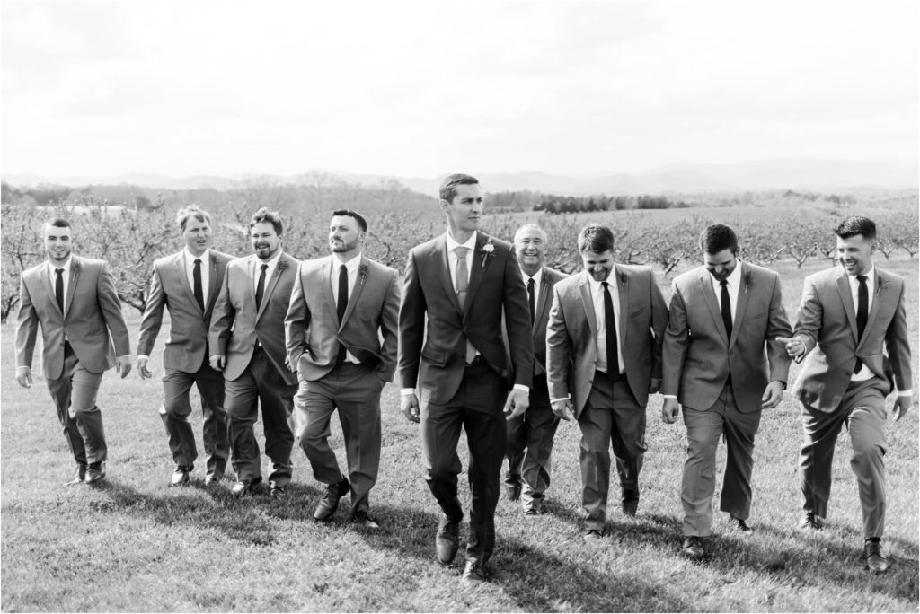 Black and white photo of groomsmen walking together across a hilltop field.