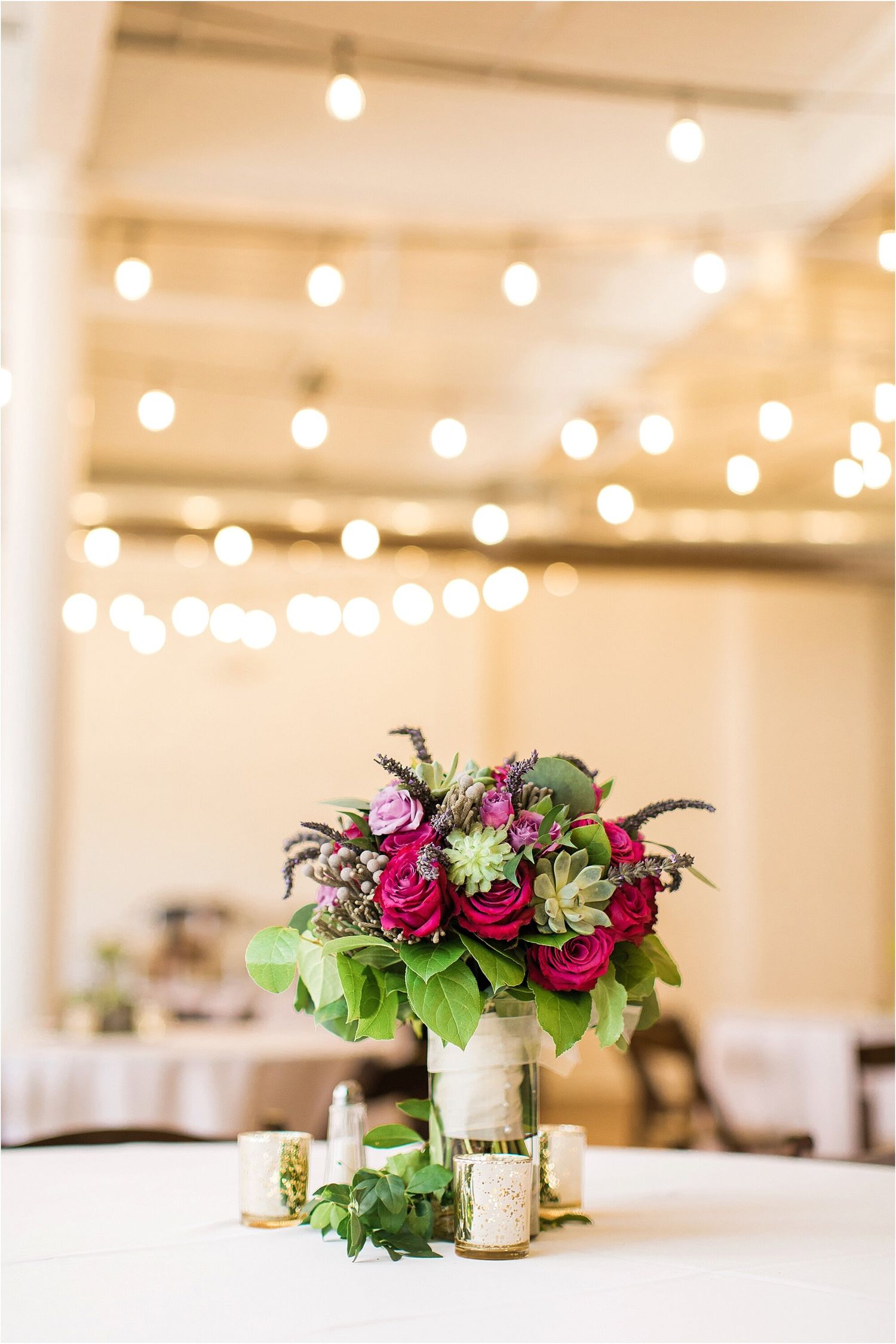 Elegant floral centerpiece with pink and burgundy blooms under string lights at wedding reception.