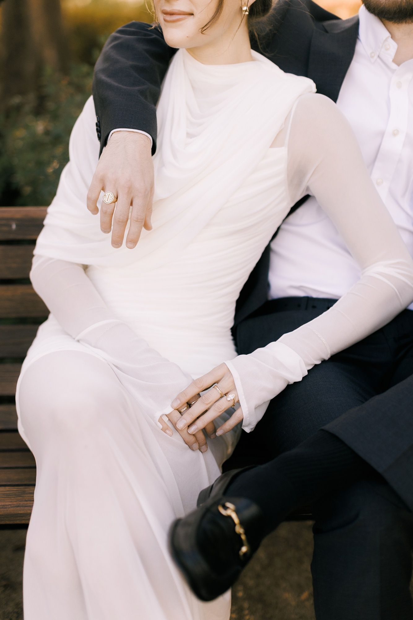Close-up detail of couple sitting together showing elegant white wedding dress with long sleeves and black formal attire.