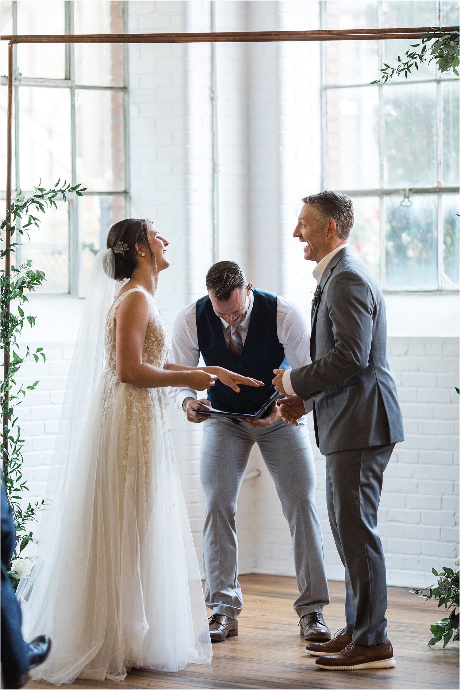 A joyful moment during the wedding ceremony with natural light streaming through tall windows.