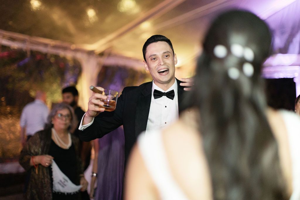 A person in a tuxedo gesturing animatedly during a wedding celebration.