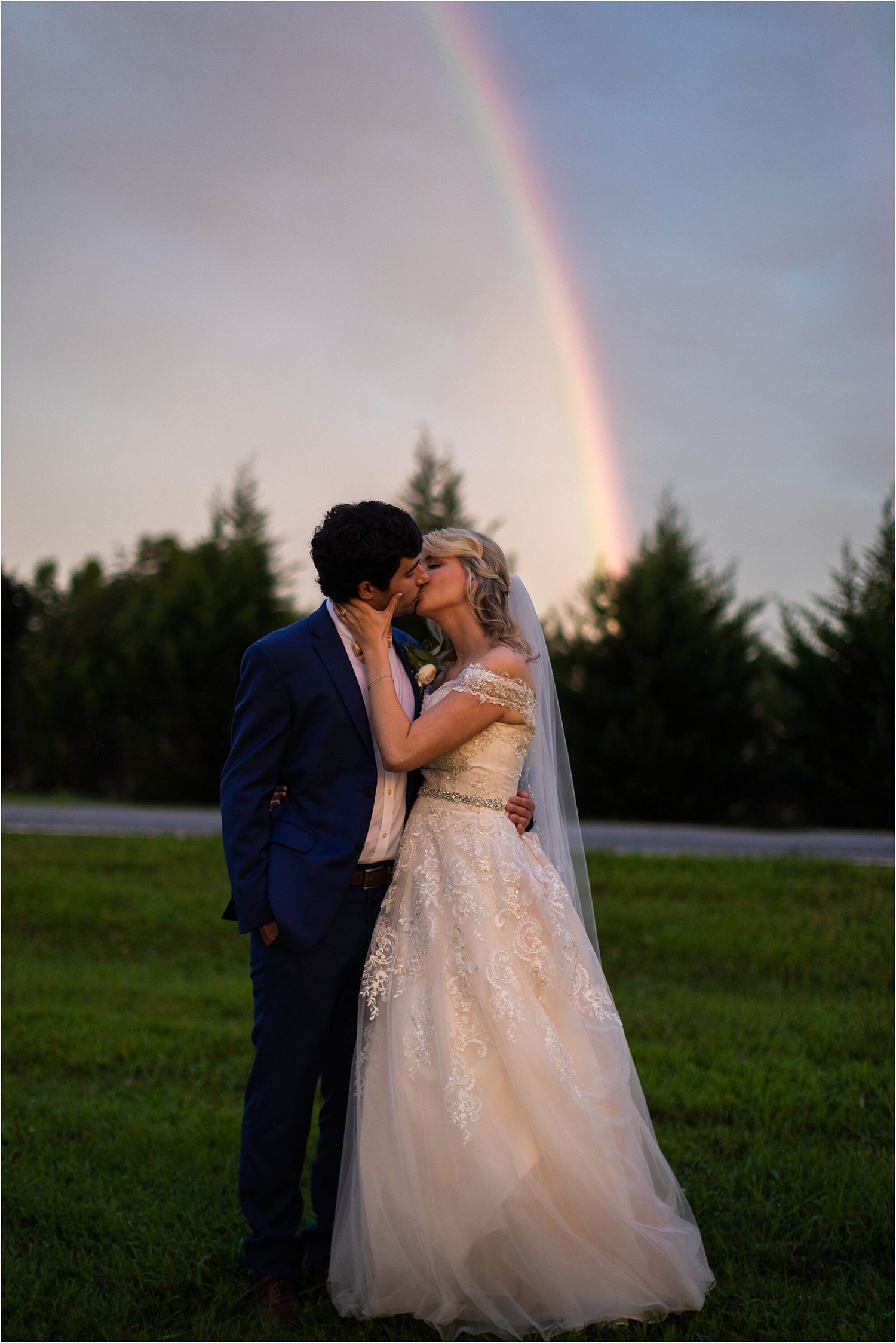 A couple embraces under a rainbow during their wedding photoshoot in an outdoor setting.