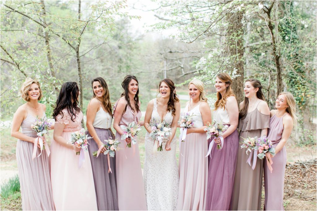 Bridesmaids in flowing pastel dresses pose together on a forest path.