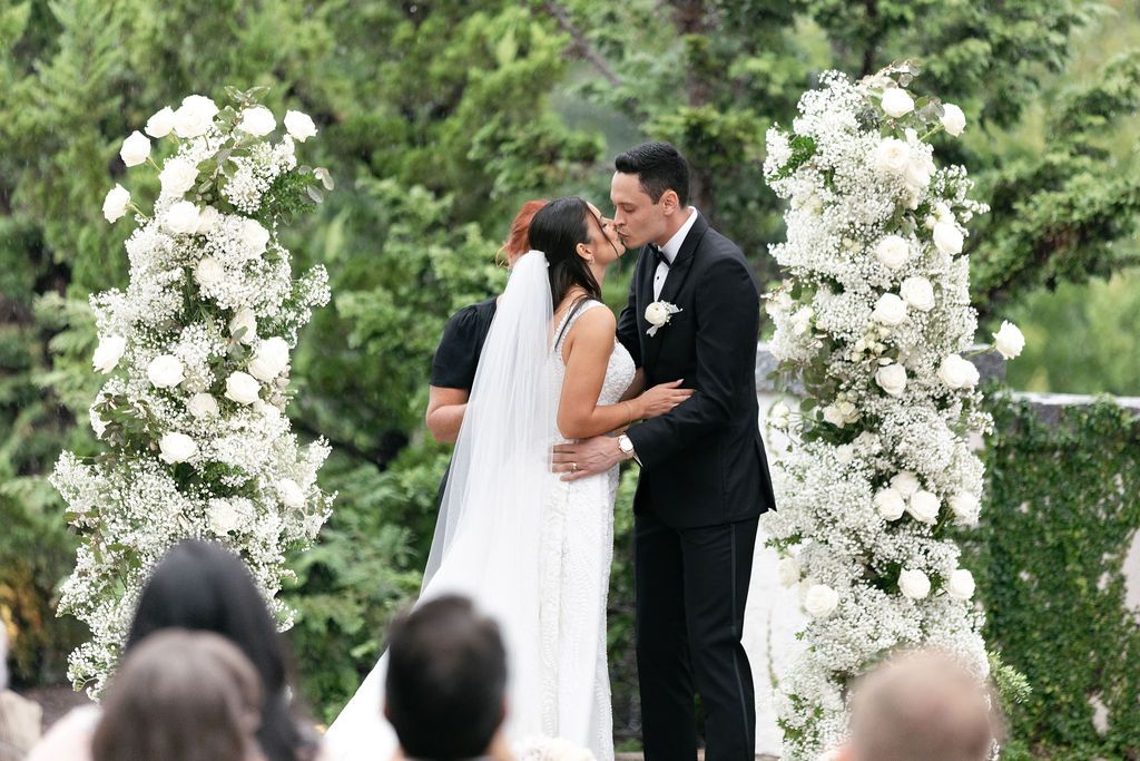 Wedding ceremony kiss under elegant white floral arches.