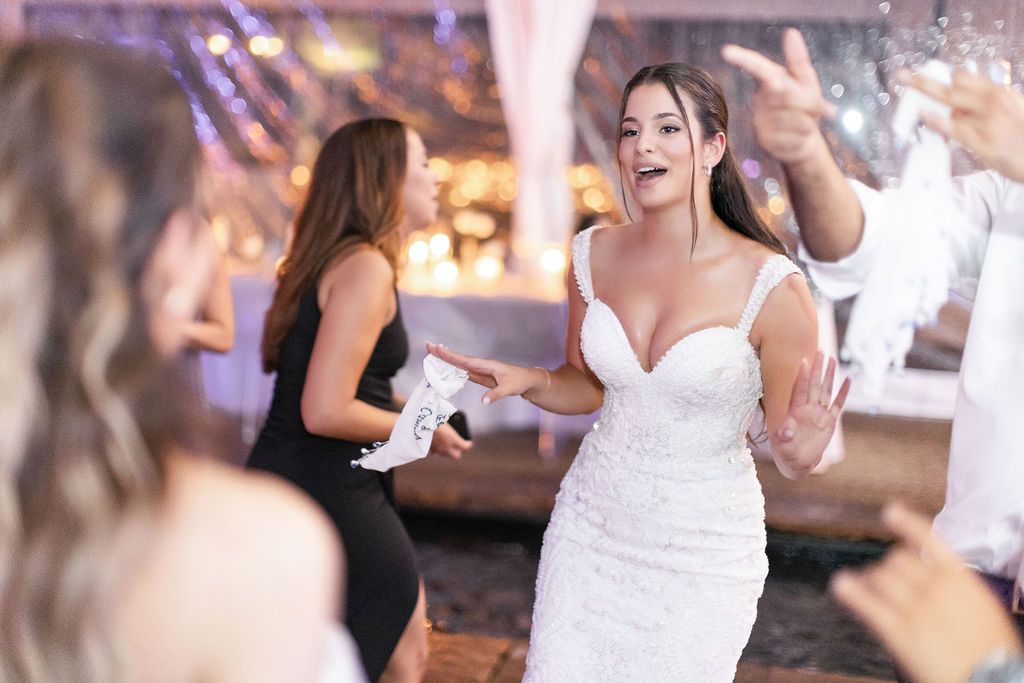 Wedding reception guests dancing and celebrating under atmospheric tent lighting.
