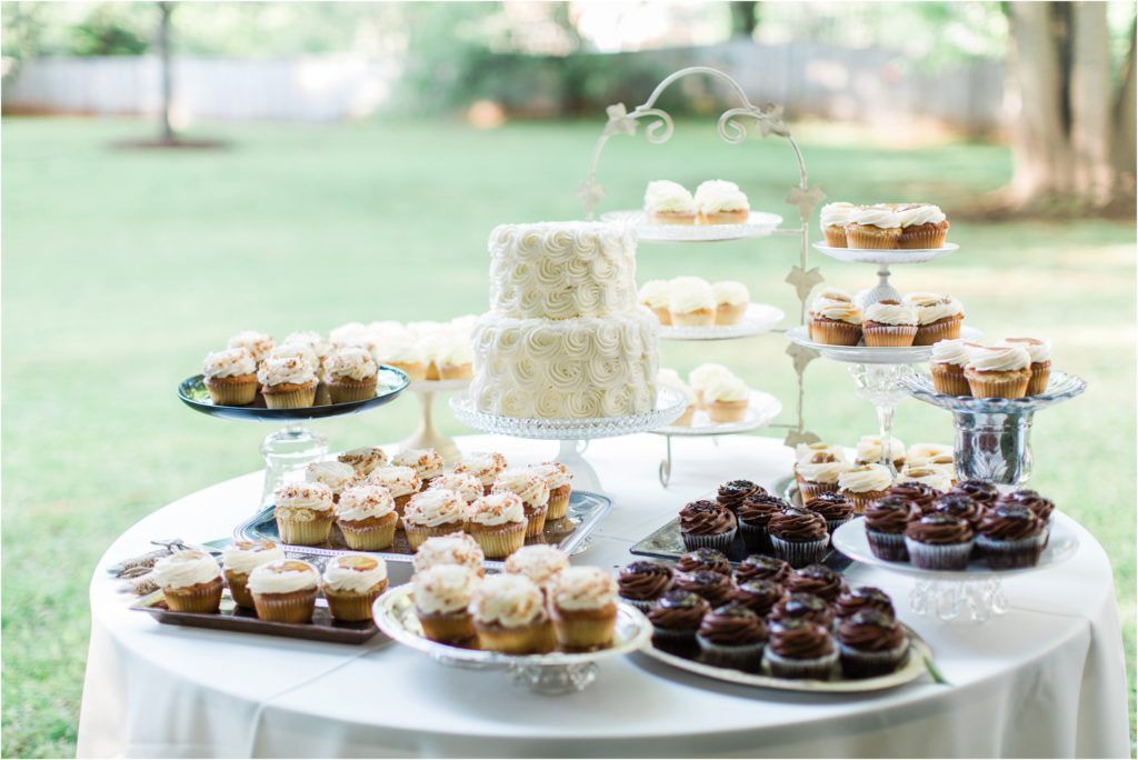 An elegant dessert table at an outdoor wedding featuring a white tiered cake and various cupcakes on display.