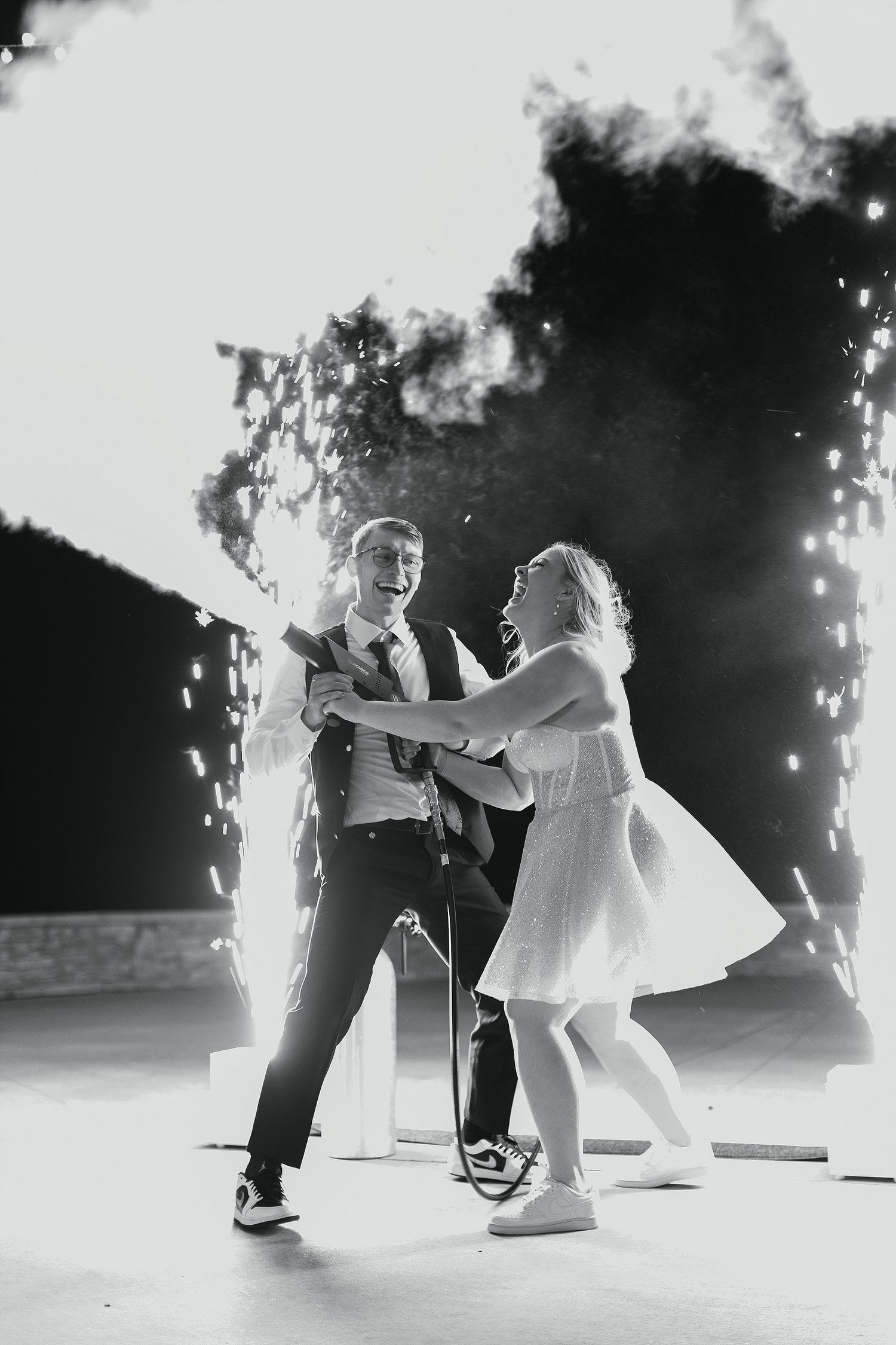 A couple dances joyfully in front of cascading sparklers during an evening celebration, captured in black and white.