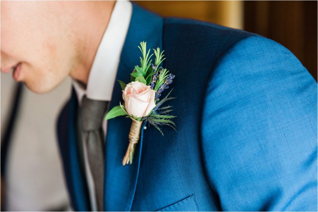 A delicate pink rose and greenery boutonniere pinned to a bright blue suit jacket.